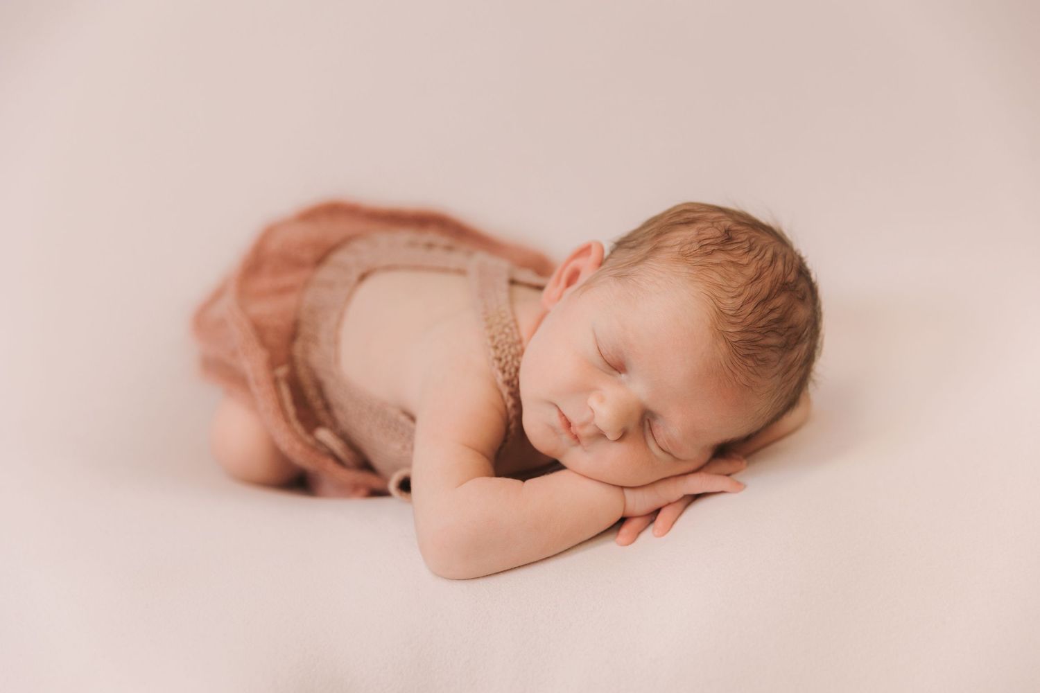 A sleeping newborn baby lies peacefully on a soft beige blanket in a series of delicate poses.