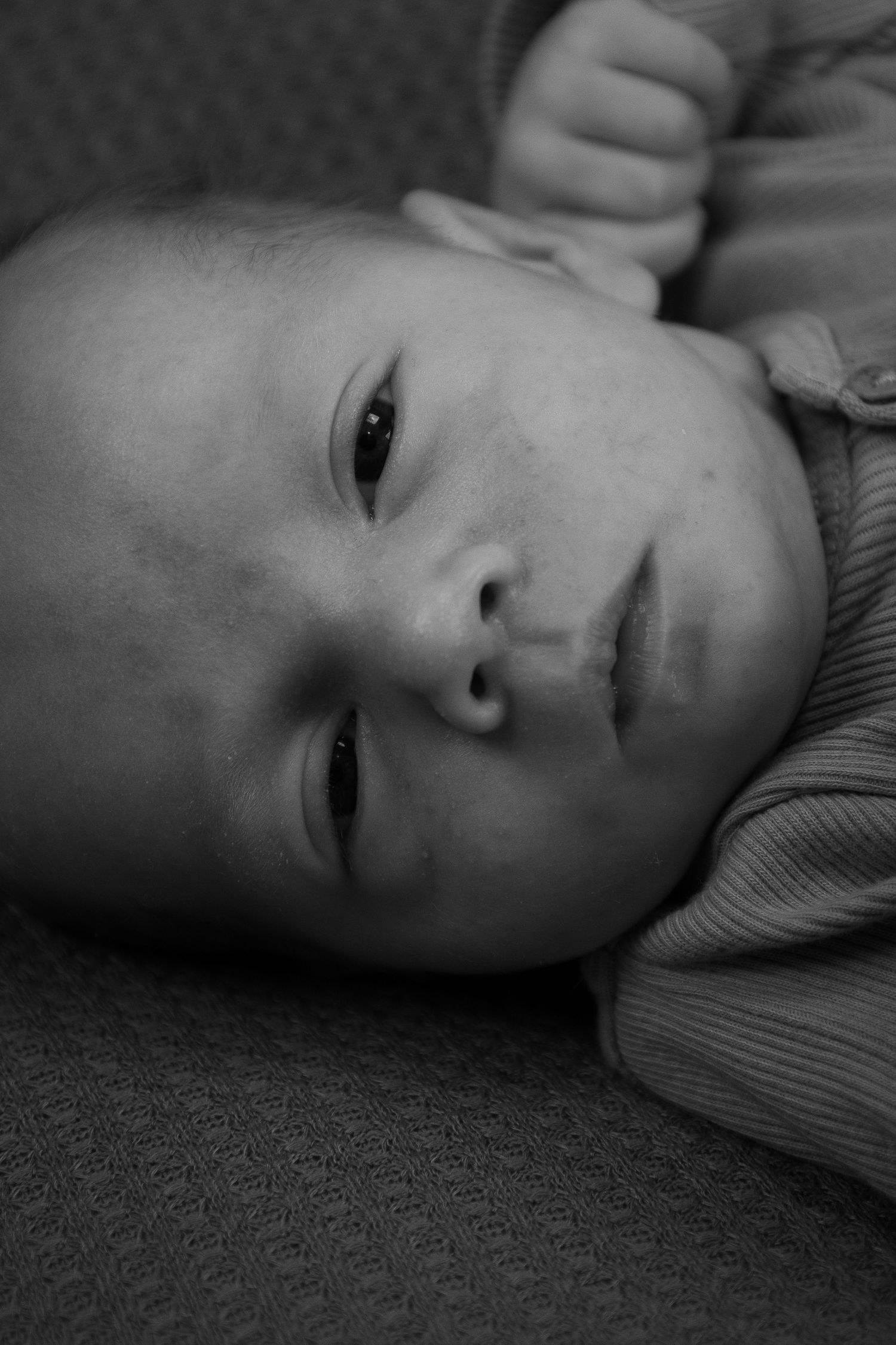Black and white close-up portrait of an infant lying on textured fabric.