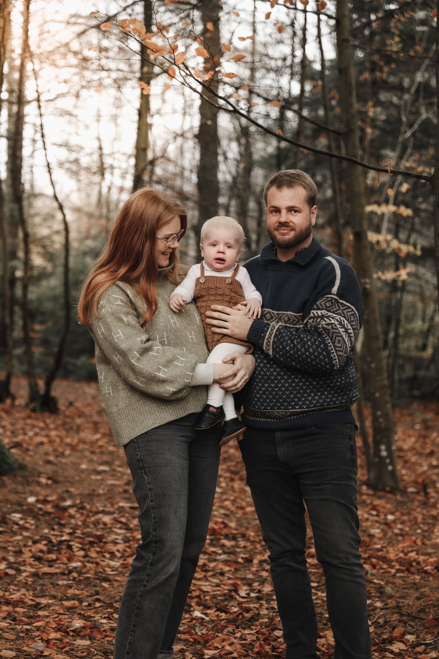 A cozy autumn family portrait in a forest with fallen leaves covering the ground.