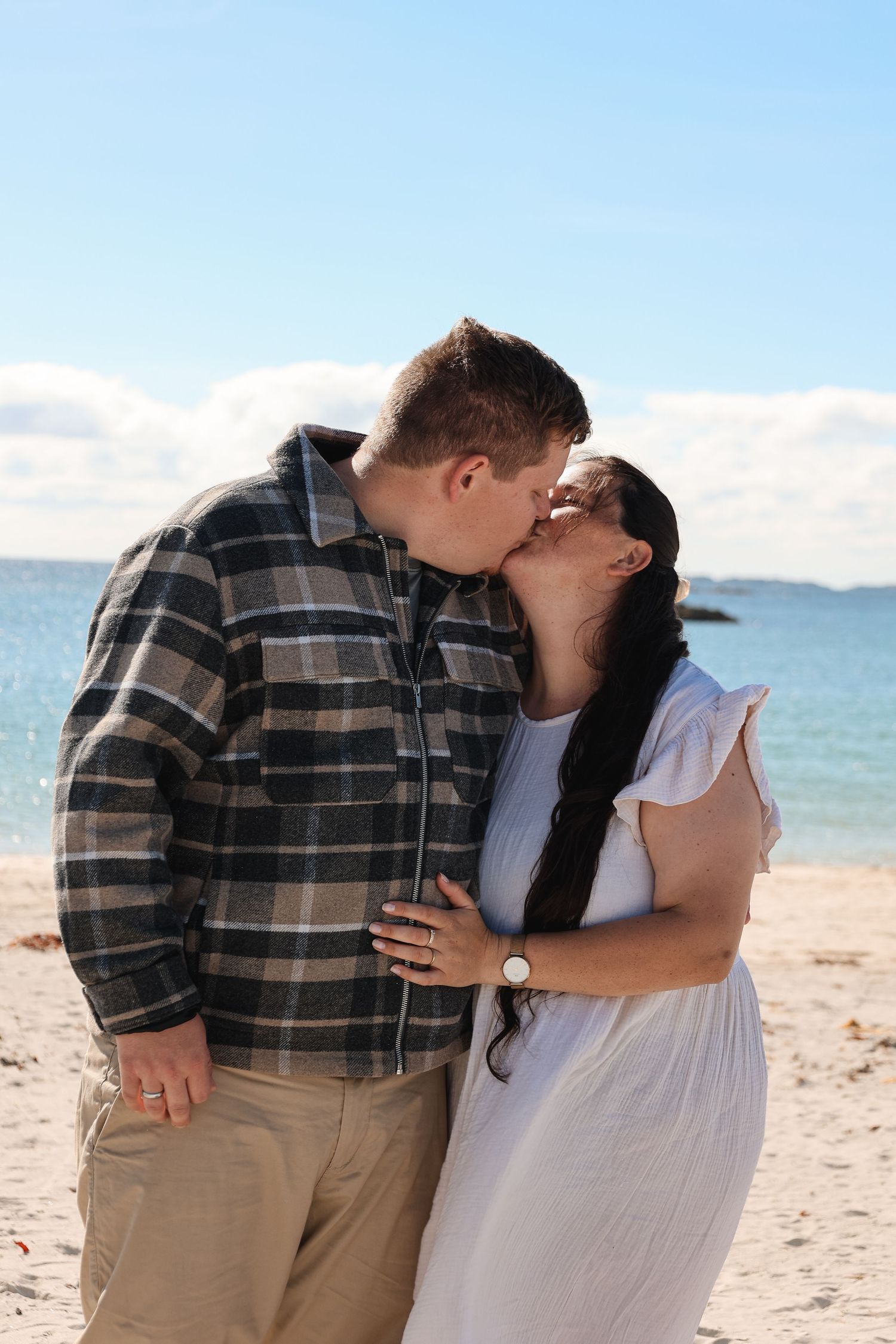 Romantic couple sharing a kiss on a sunny beach with ocean views.
