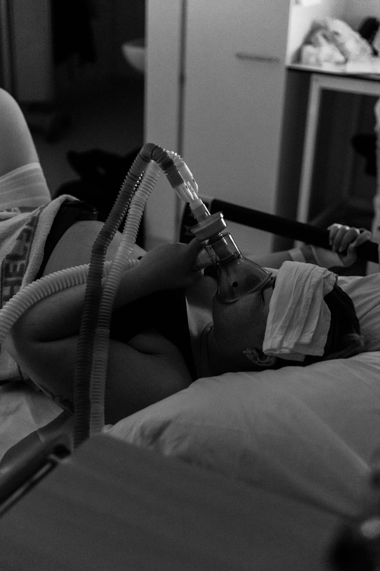 Black and white image of someone lying in a hospital bed wearing a CPAP breathing mask.