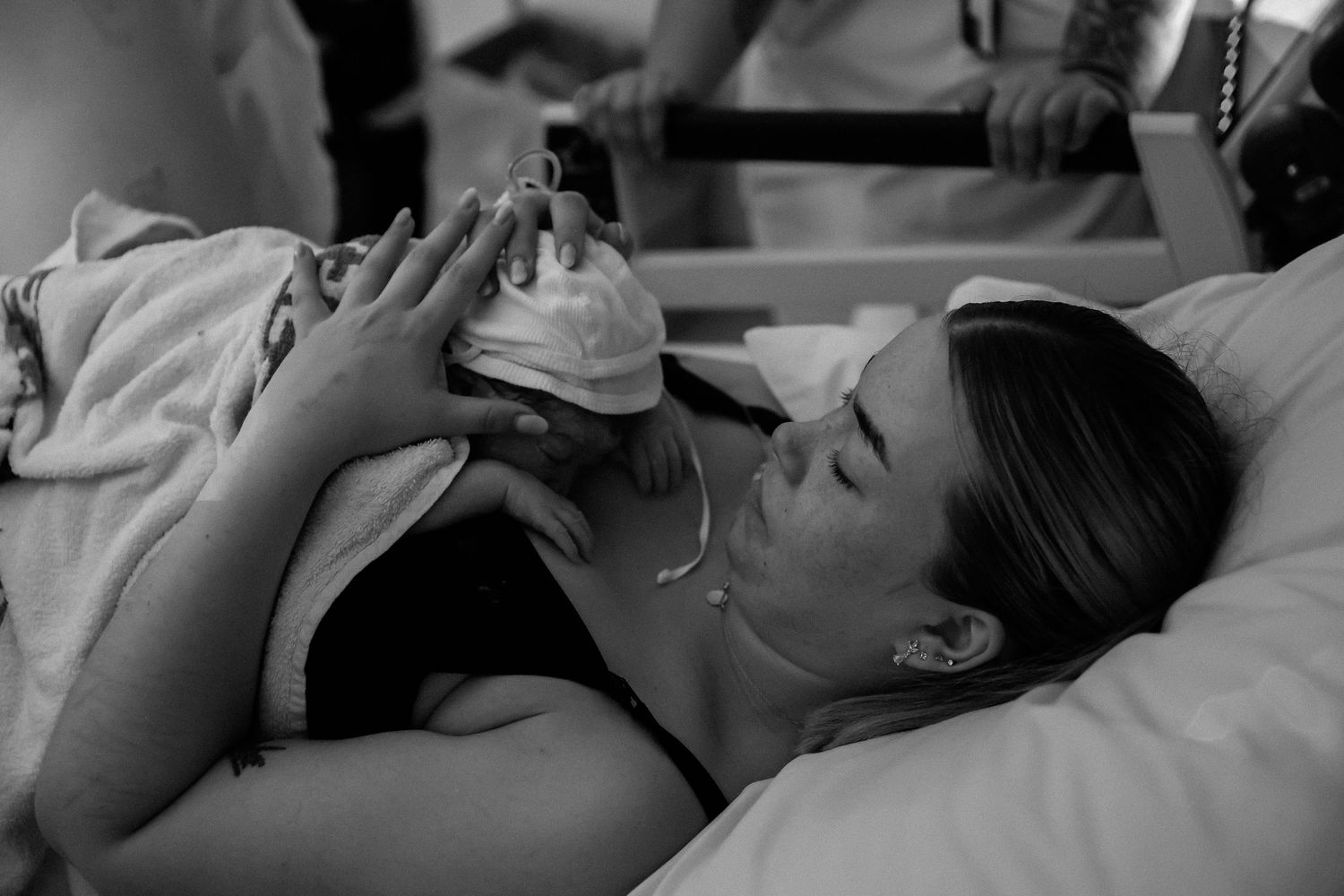 A black and white photo shows a woman lying in a hospital bed holding a small newborn baby.