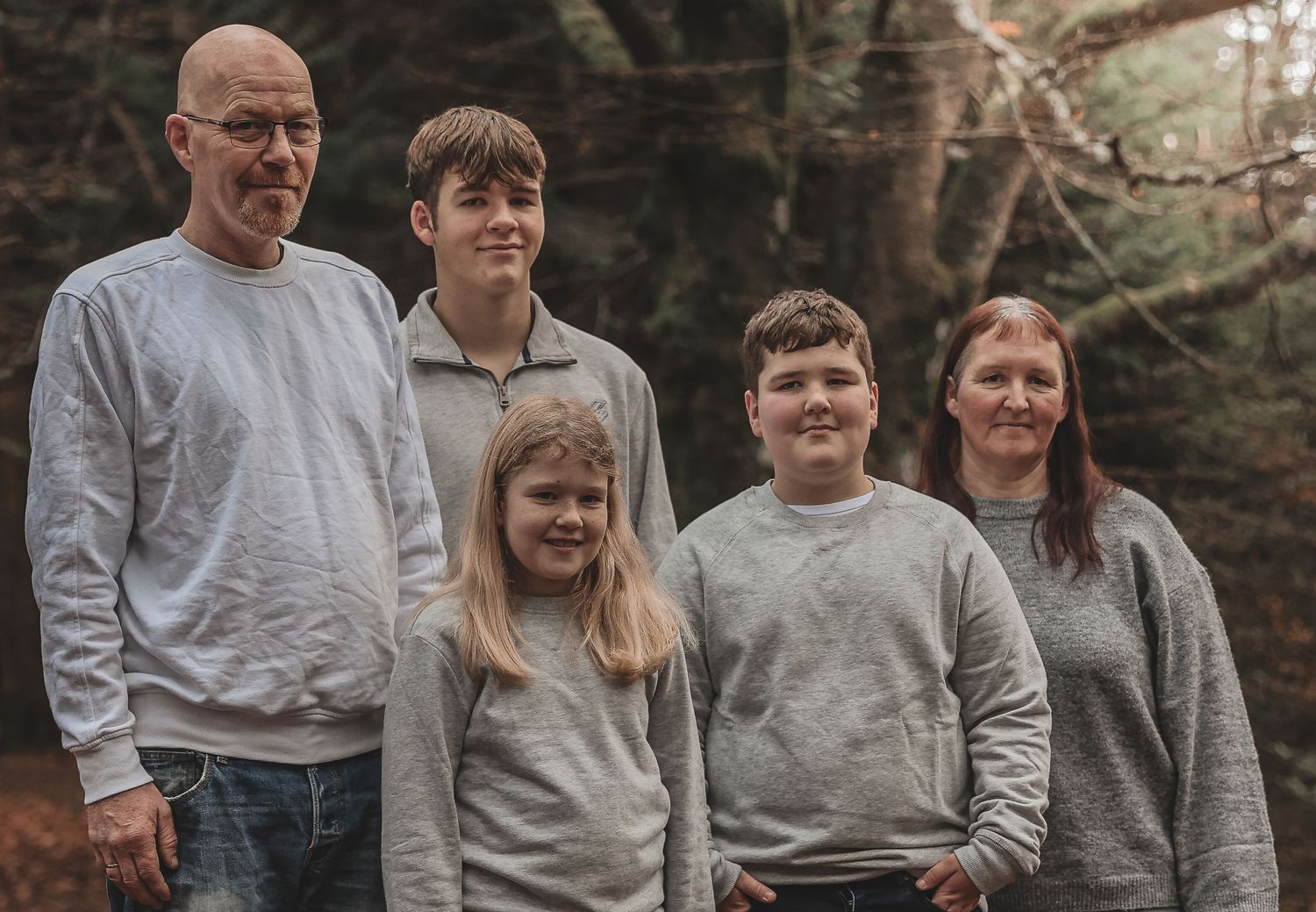 A group of five people wearing matching casual grey sweatshirts pose together outdoors during autumn.