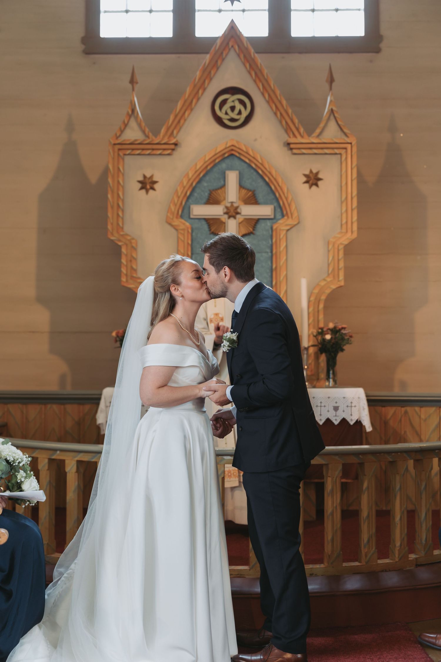 Bride and groom share first kiss at altar in a beautifully decorated wooden church during wedding ceremony.