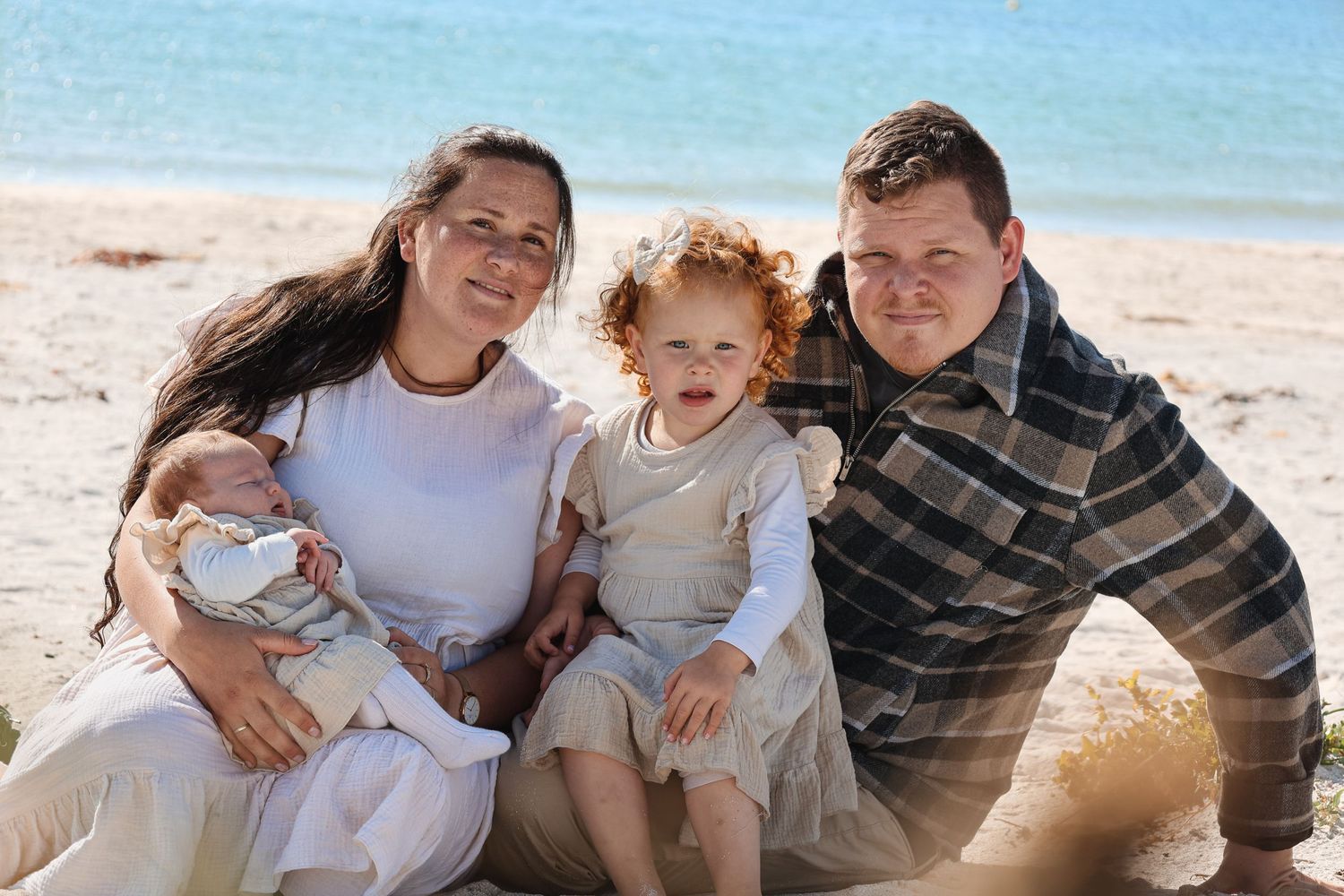 Happy family sits together smiling on sunny beach with ocean in background.