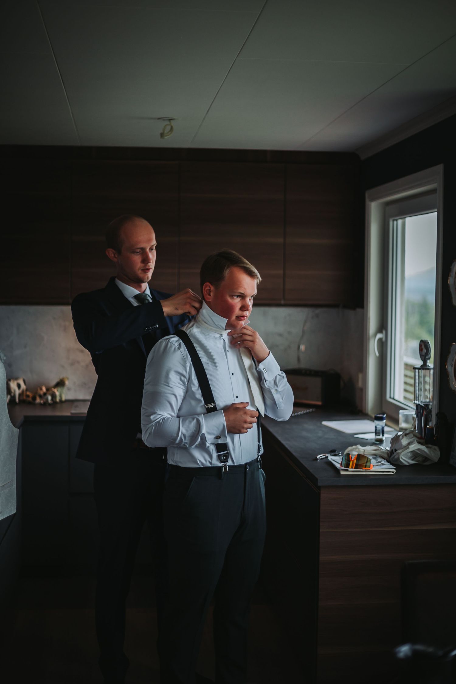 Two men in formal attire getting ready in modern kitchen before event.