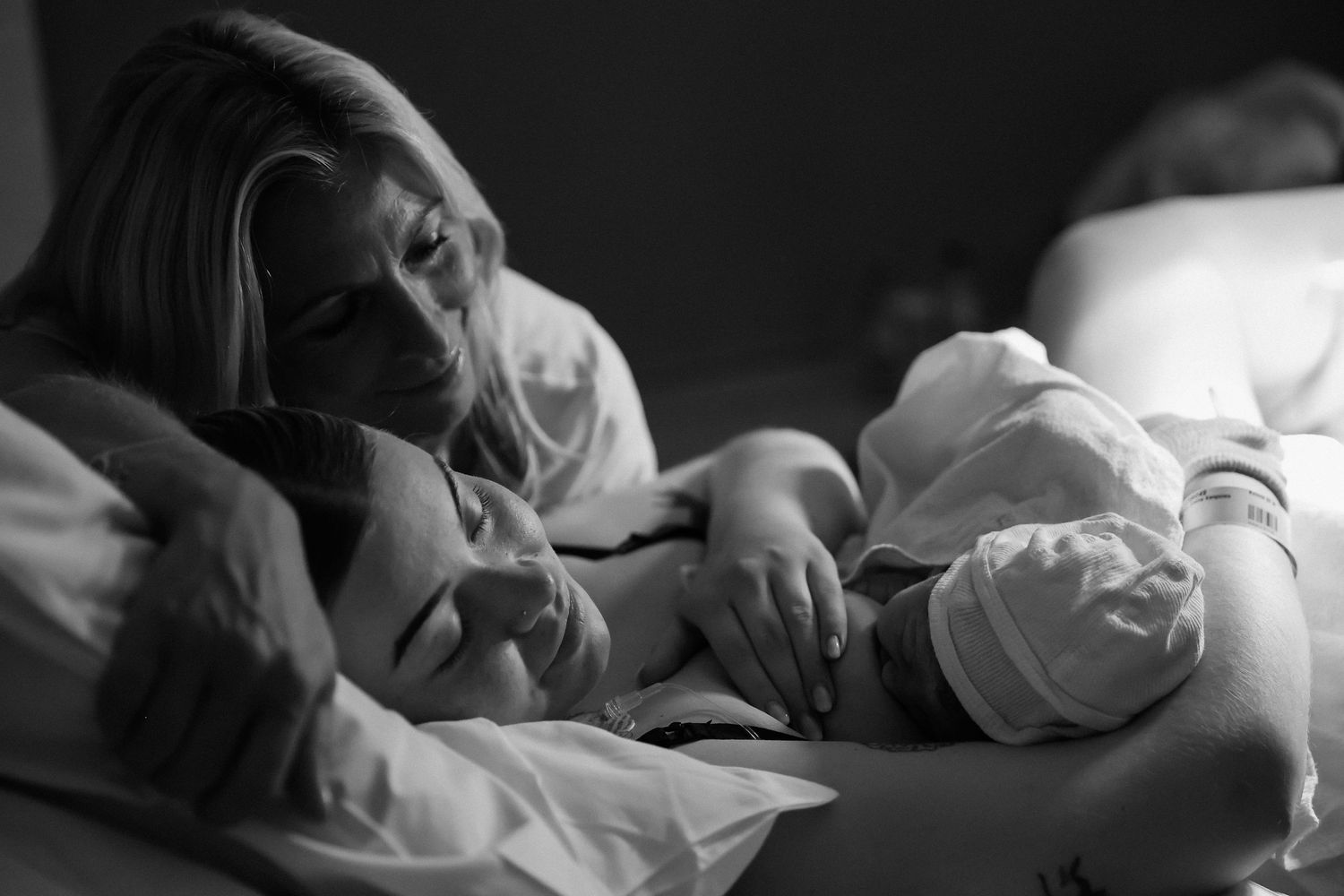Intimate black and white photo of mother and newborn resting together in bed.