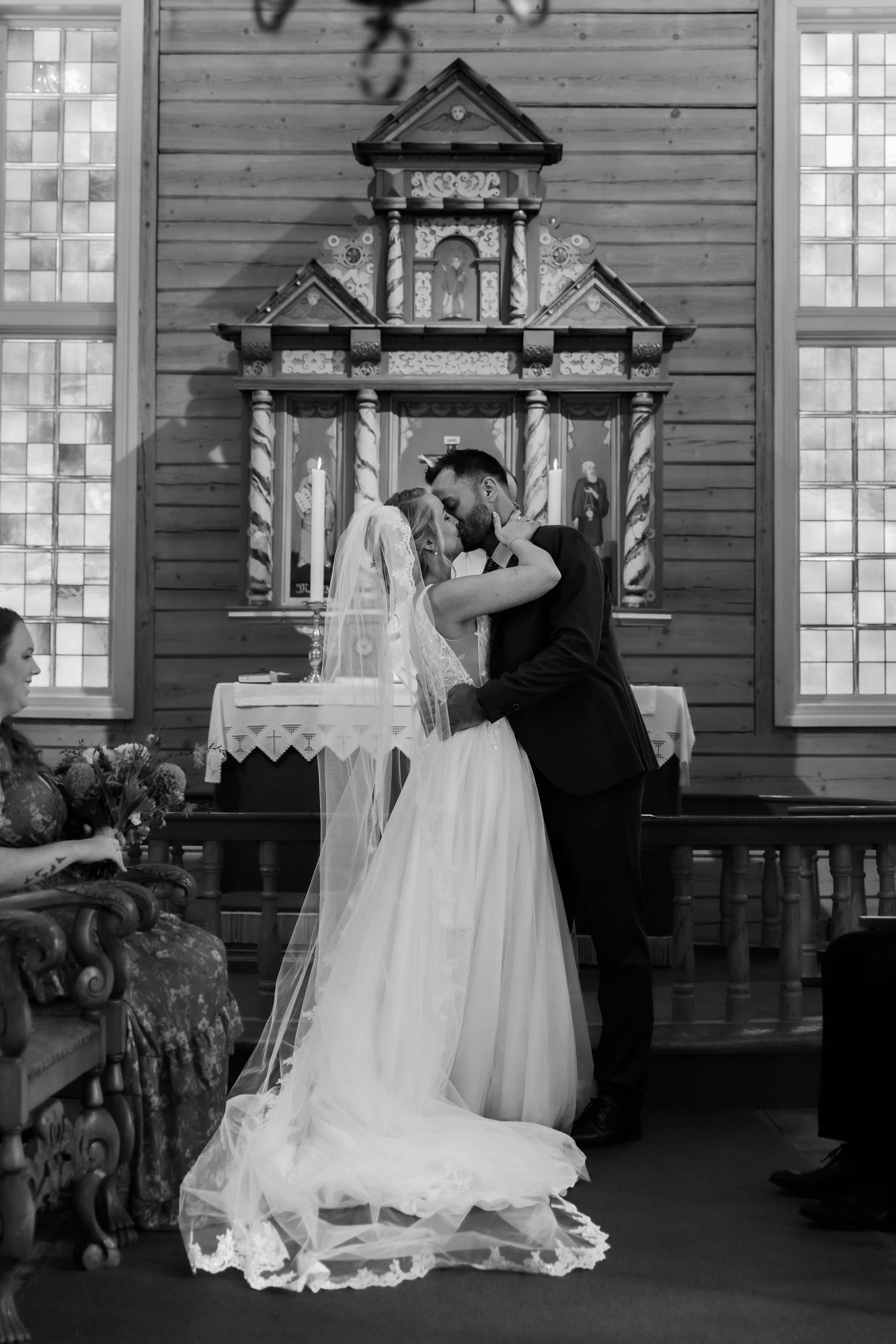 Black and white photo of a bride and groom sharing their first kiss at the altar in a historic wooden church.