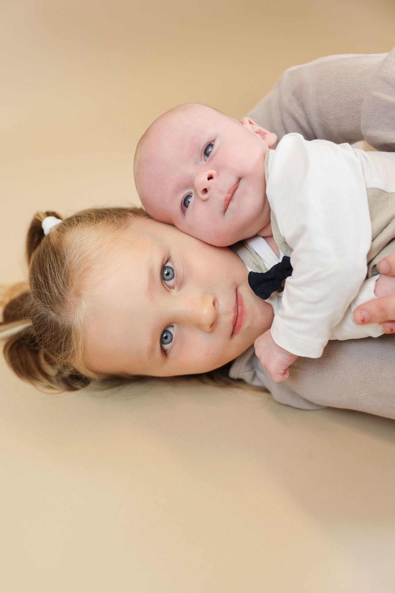 Two children lying together with bright blue eyes, one older and one baby, sharing a tender sibling moment.