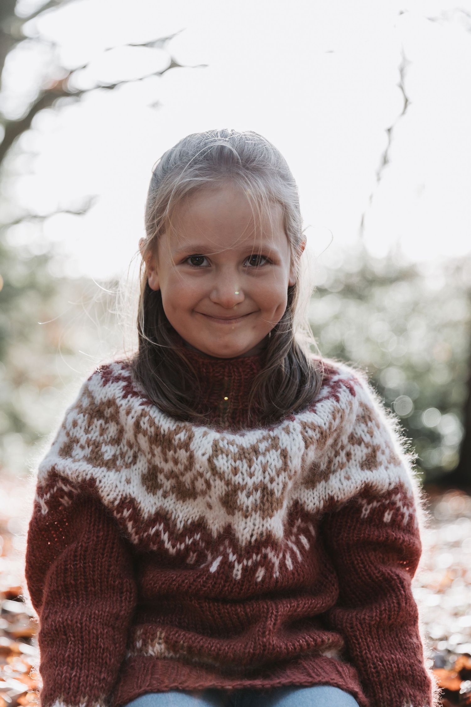 A person wearing a cozy burgundy and white Fair Isle knit sweater smiles warmly during a winter photo session.
