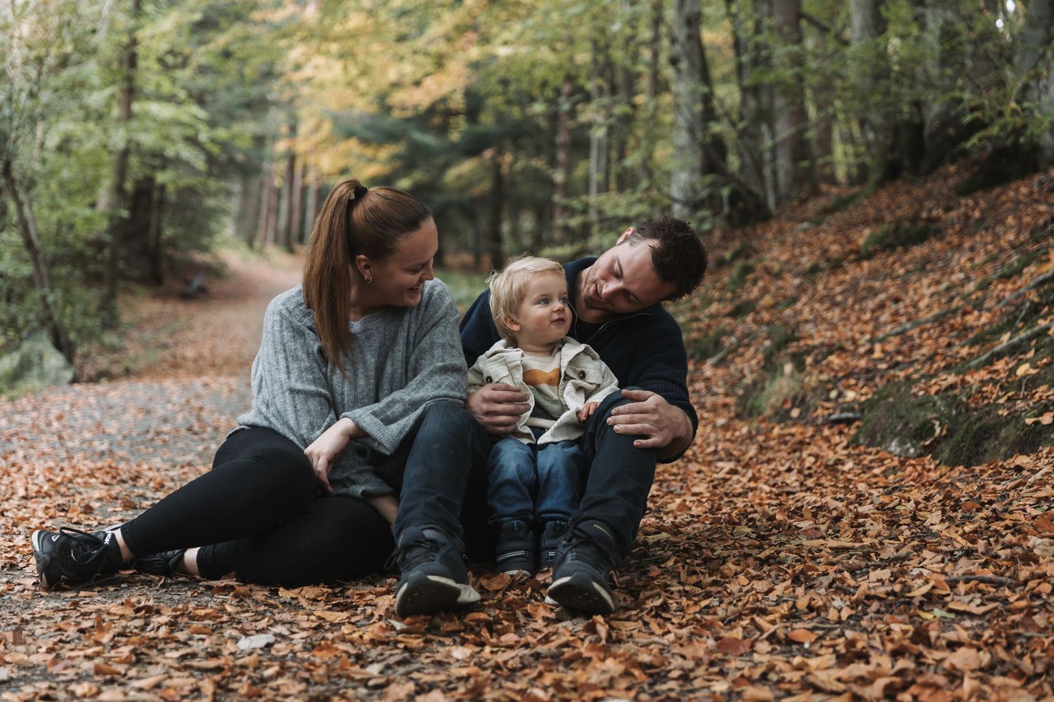 A joyful family moment captured while sitting on autumn leaves in a forest setting.