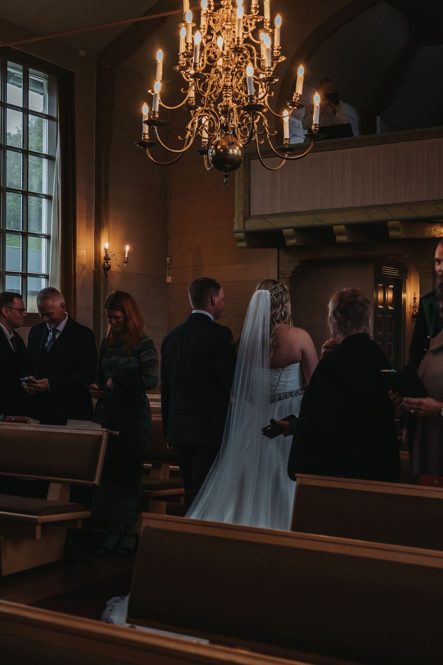 Wedding ceremony in traditional church with elegant chandelier and wooden pews.