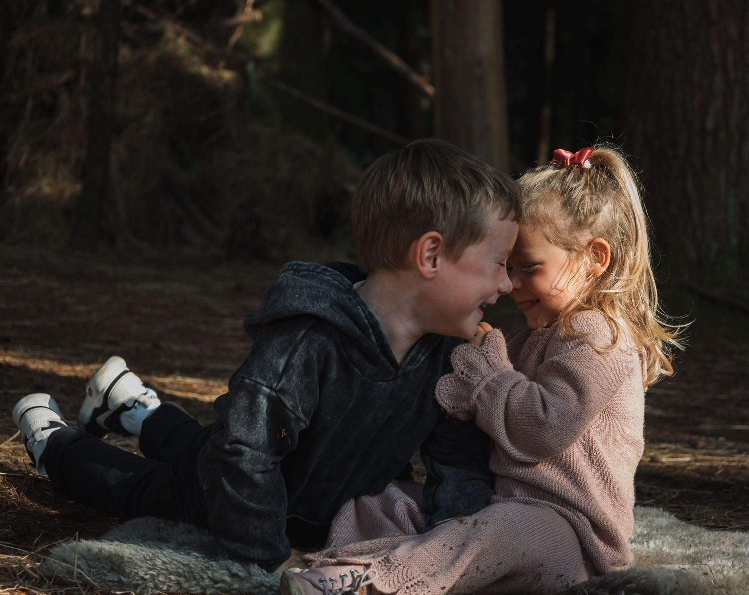 Intimate and playful moment captured between two siblings in a dark forest setting.