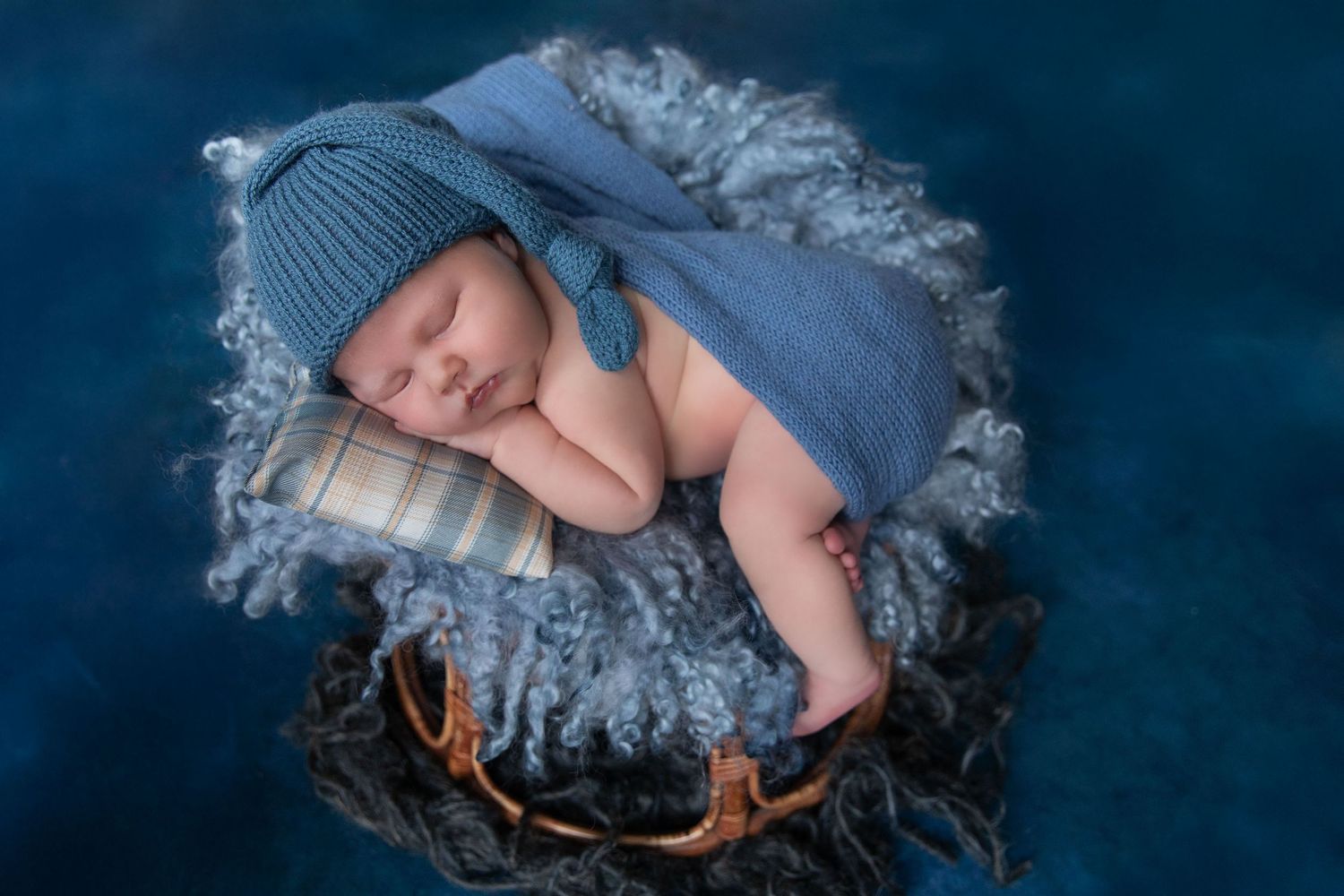 Newborn baby sleeping peacefully in a blue knit hat and wrap, nestled in a rustic basket with antlers.