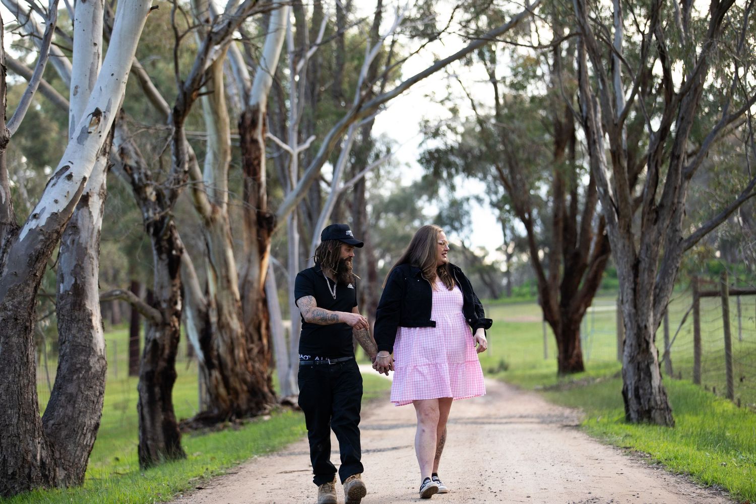 Couple walking hand in hand down a tree-lined dirt path surrounded by eucalyptus trees and green grass.