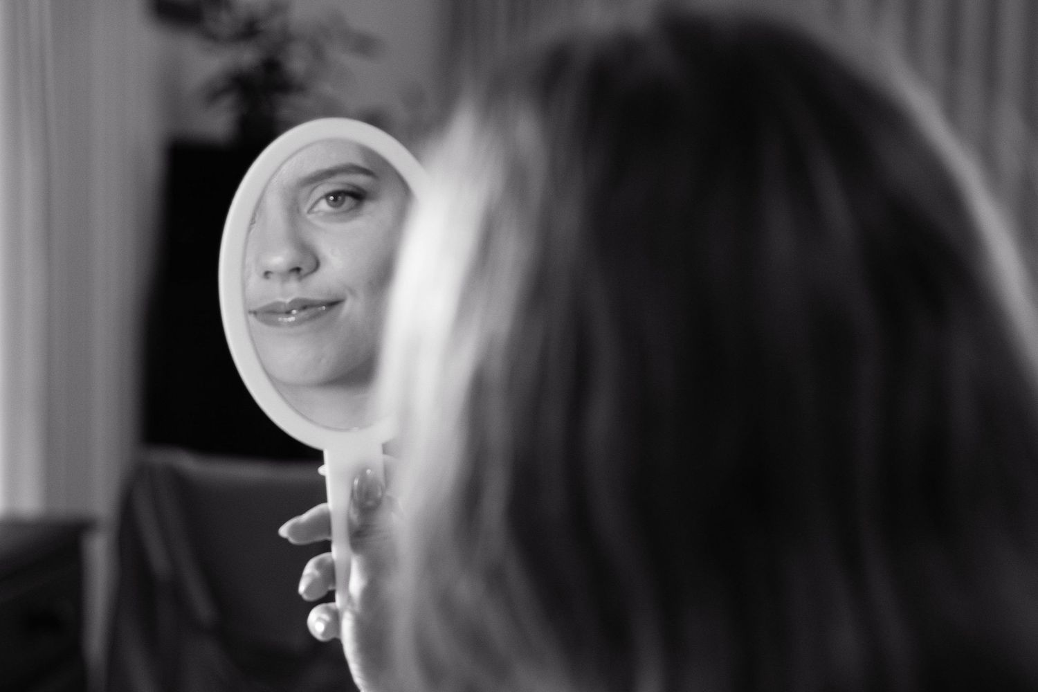 Woman gazing at her reflection in a small handheld mirror, captured in black and white photography.