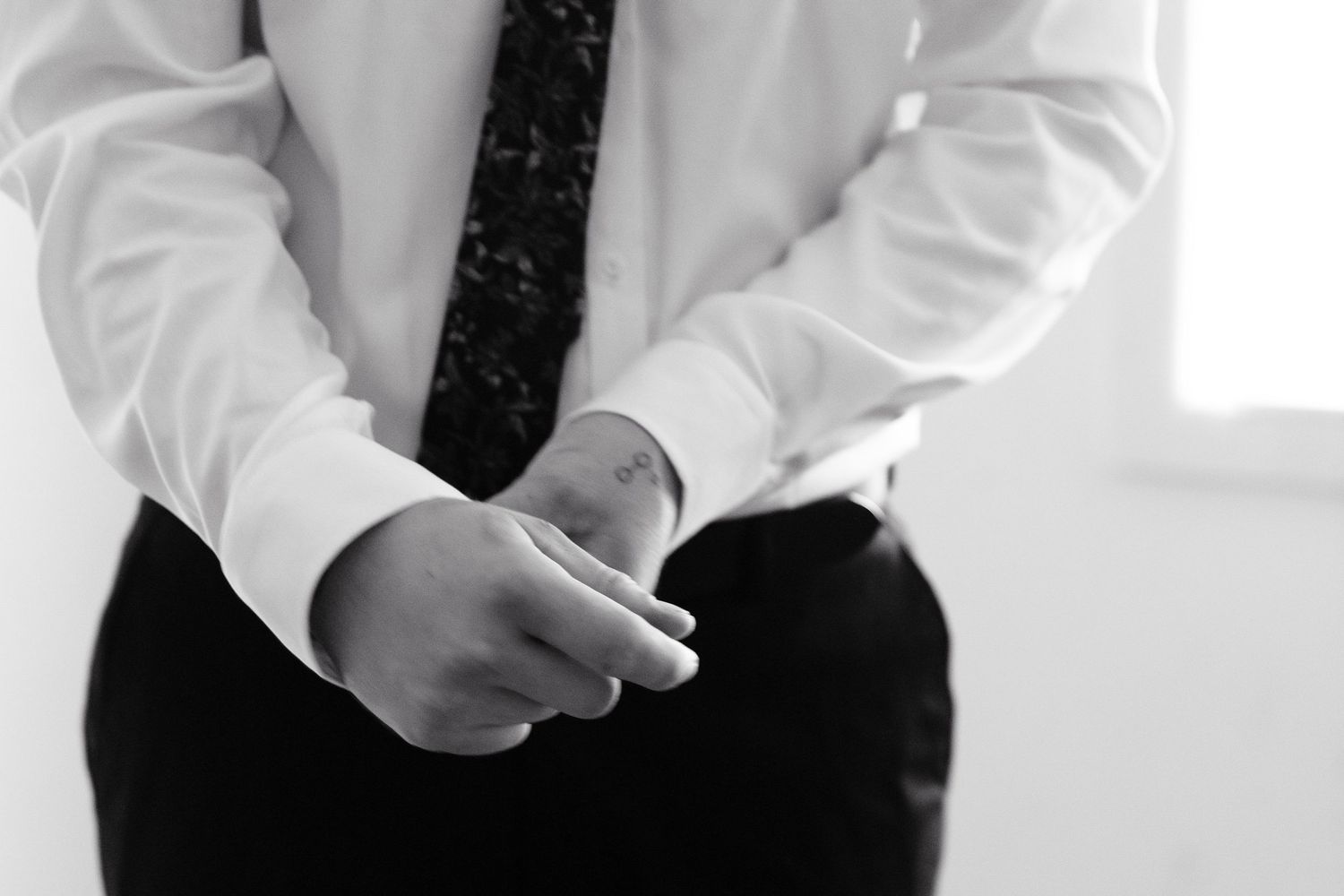 Black and white photo of a man in white dress shirt and tie adjusting his cufflinks, formal attire close-up.