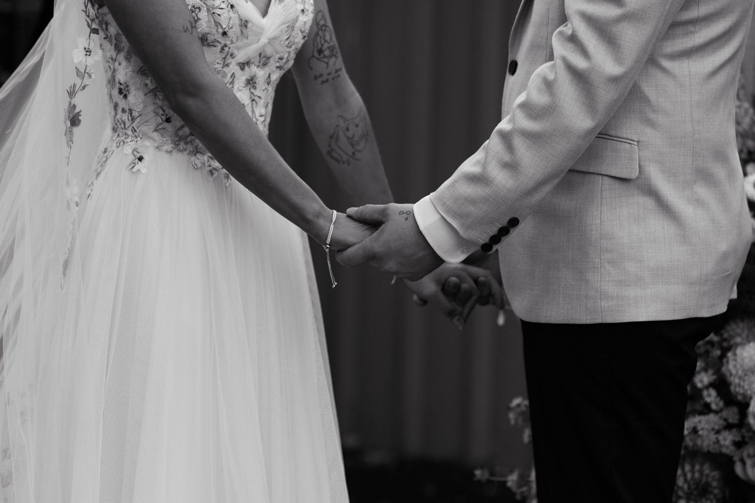 Black and white photo of a bride and groom holding hands at their wedding ceremony.