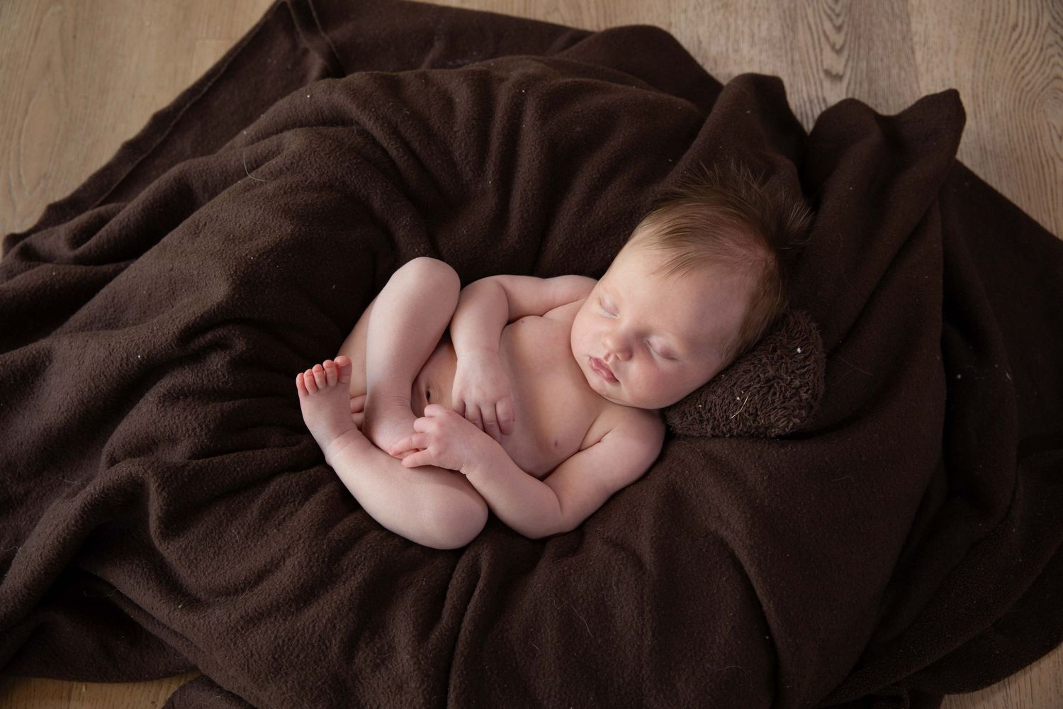 A sleeping baby lies peacefully on a brown blanket in a series of connected newborn portraits.