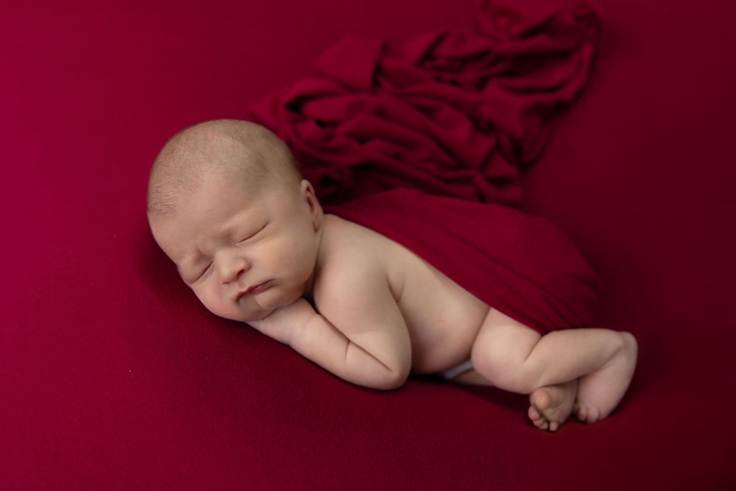 Peaceful newborn baby sleeping on red fabric backdrop in professional newborn photography session.