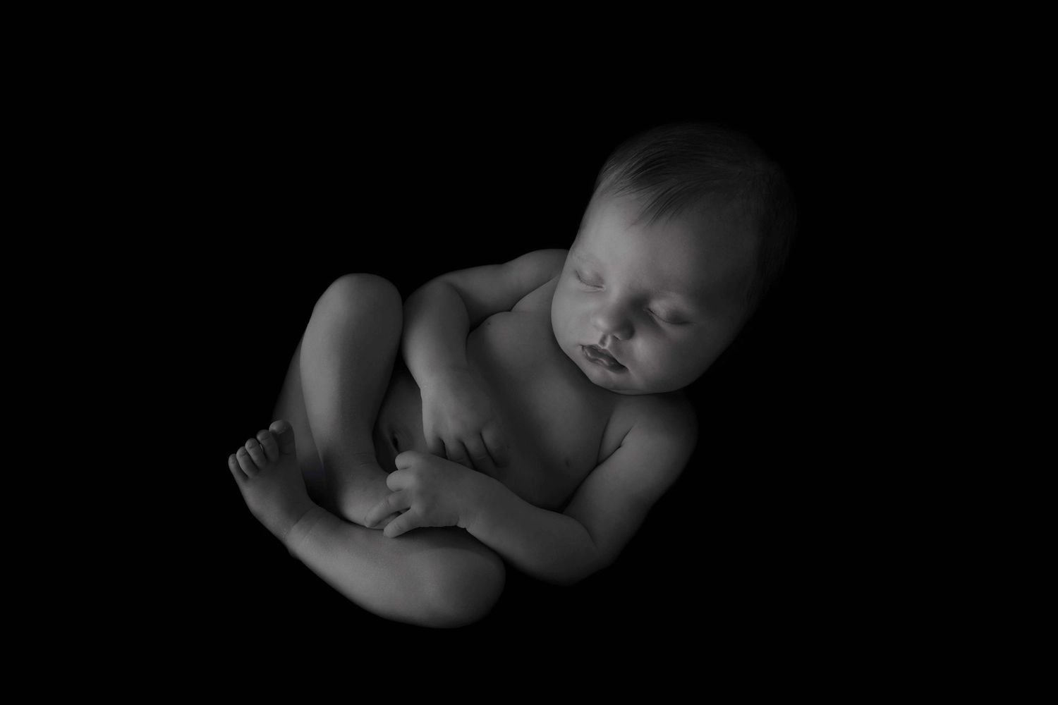 A series of black and white close-up photographs showing parts of a sleeping baby in dramatic lighting.