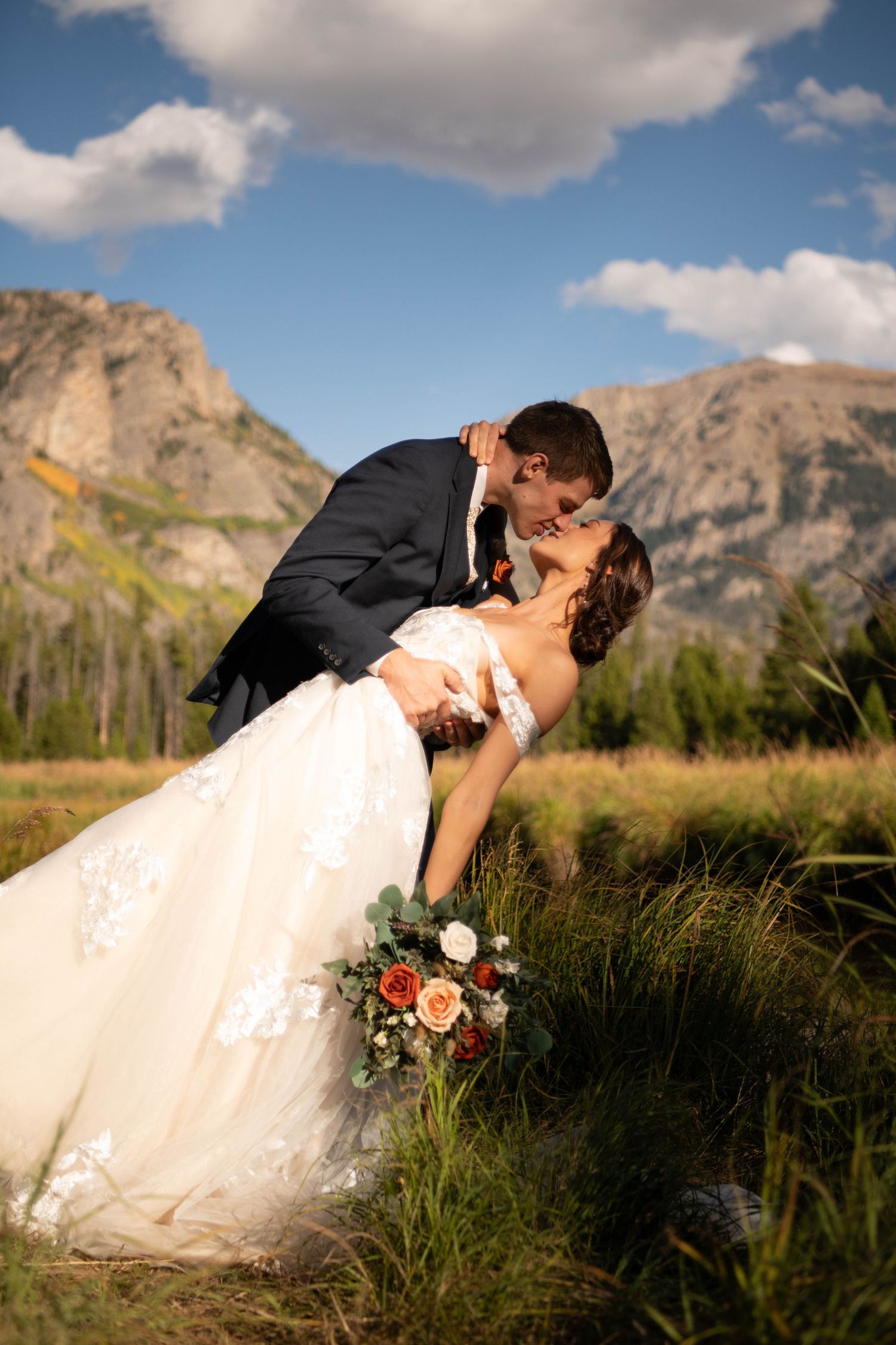 A romantic dip pose with mountains and wildflowers in the background.