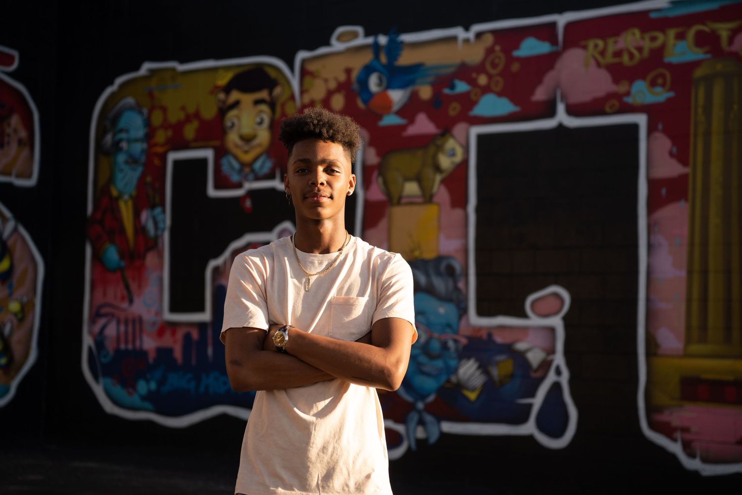 Portrait of person in white t-shirt standing against colorful graffiti wall at sunset.