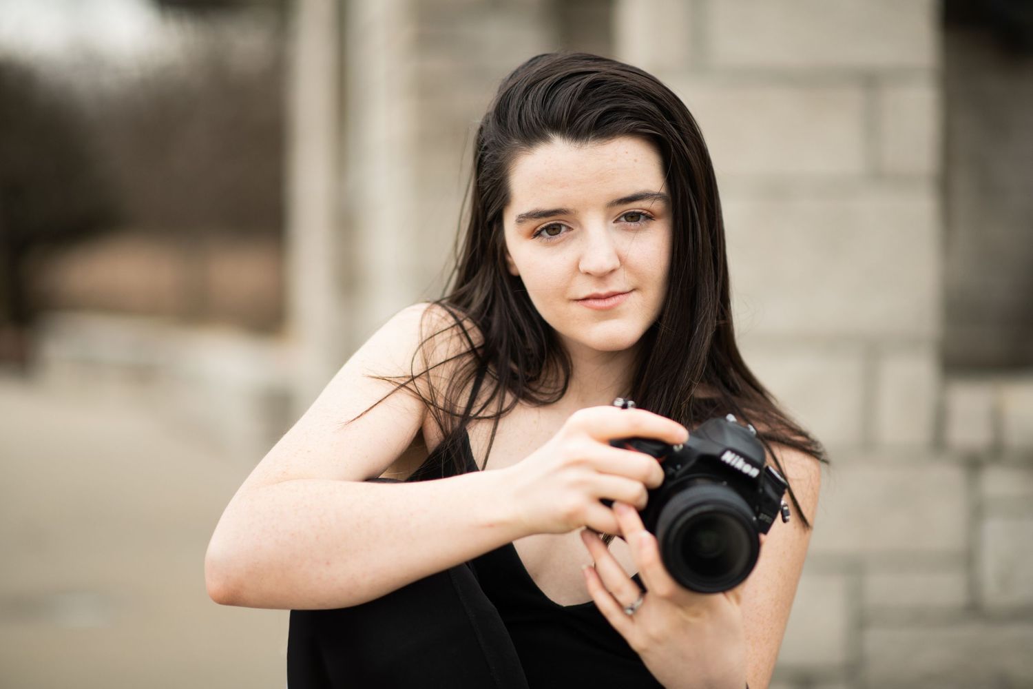 Young photographer holding DSLR camera outdoors with soft focus background.