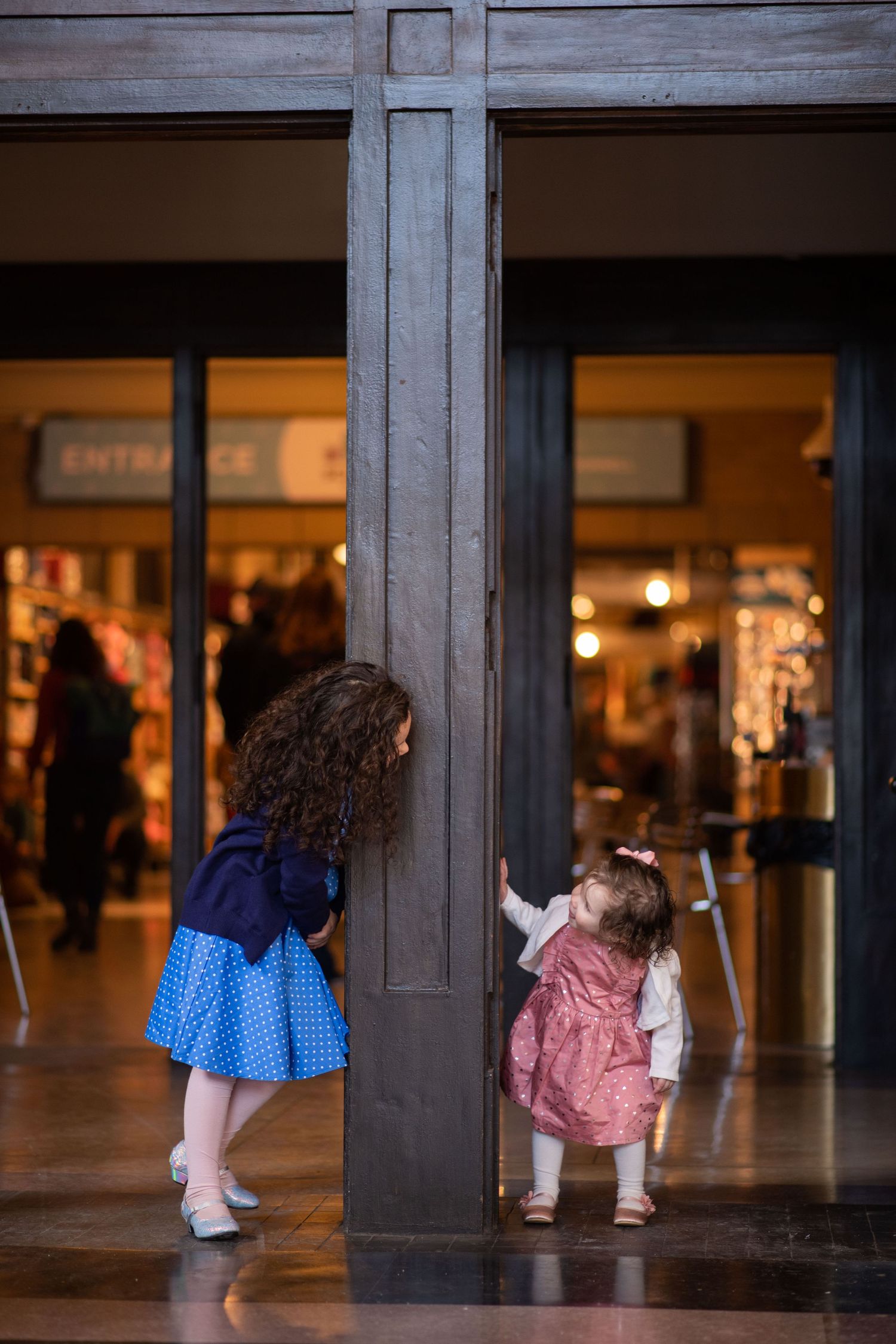 Two young children in dresses exploring storefront window display.