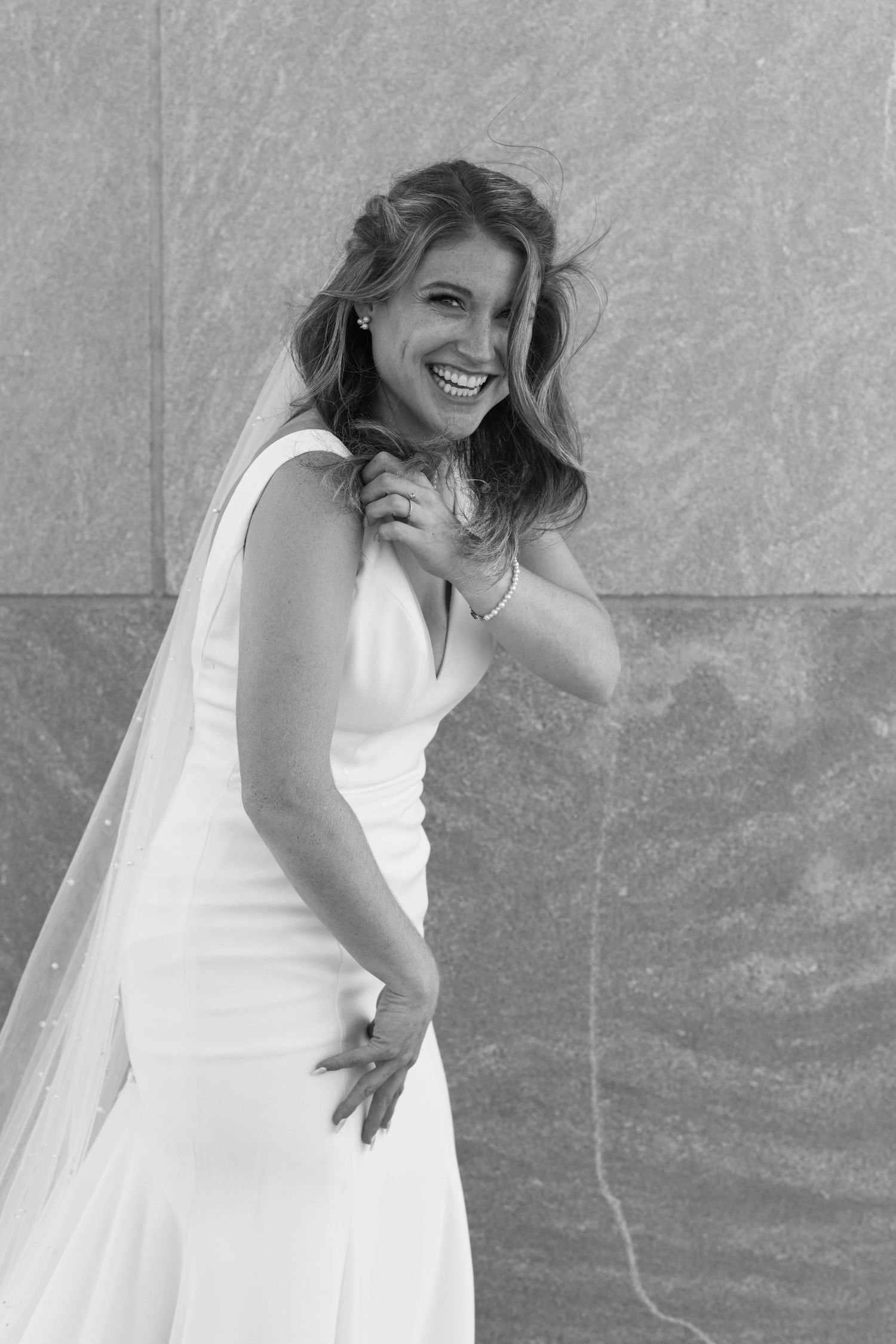 A bride in a white wedding dress poses against a textured wall.