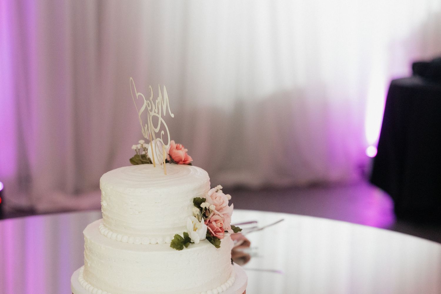 An elegant white wedding cake decorated with delicate pink flowers sits on display.