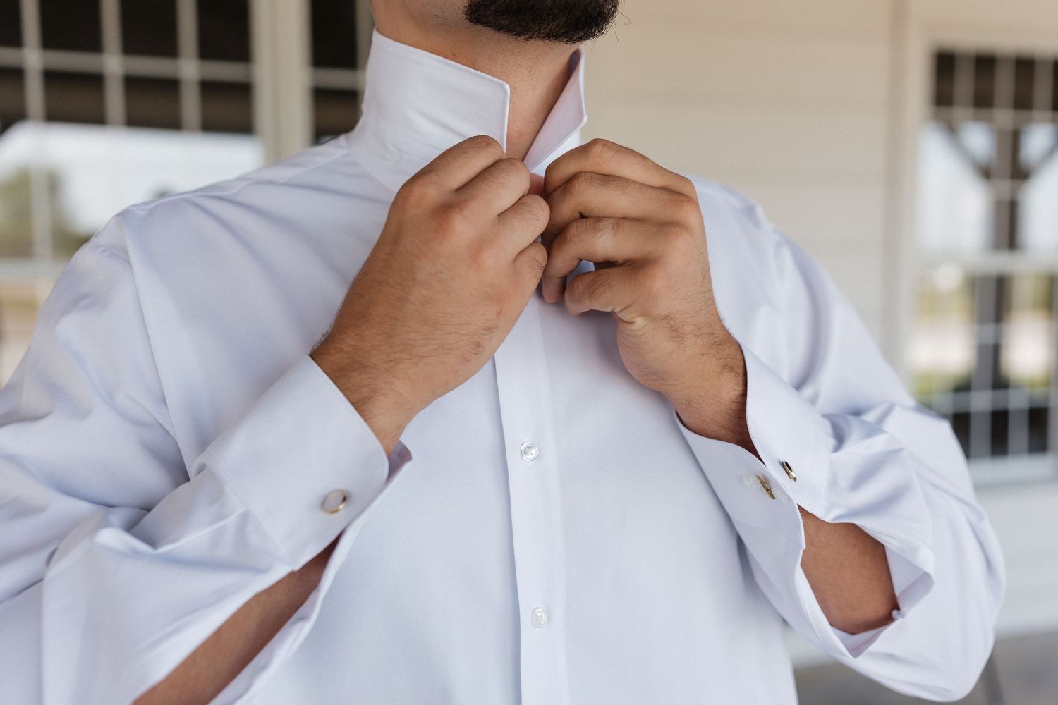 Man adjusting white dress shirt collar and red tie while getting dressed.