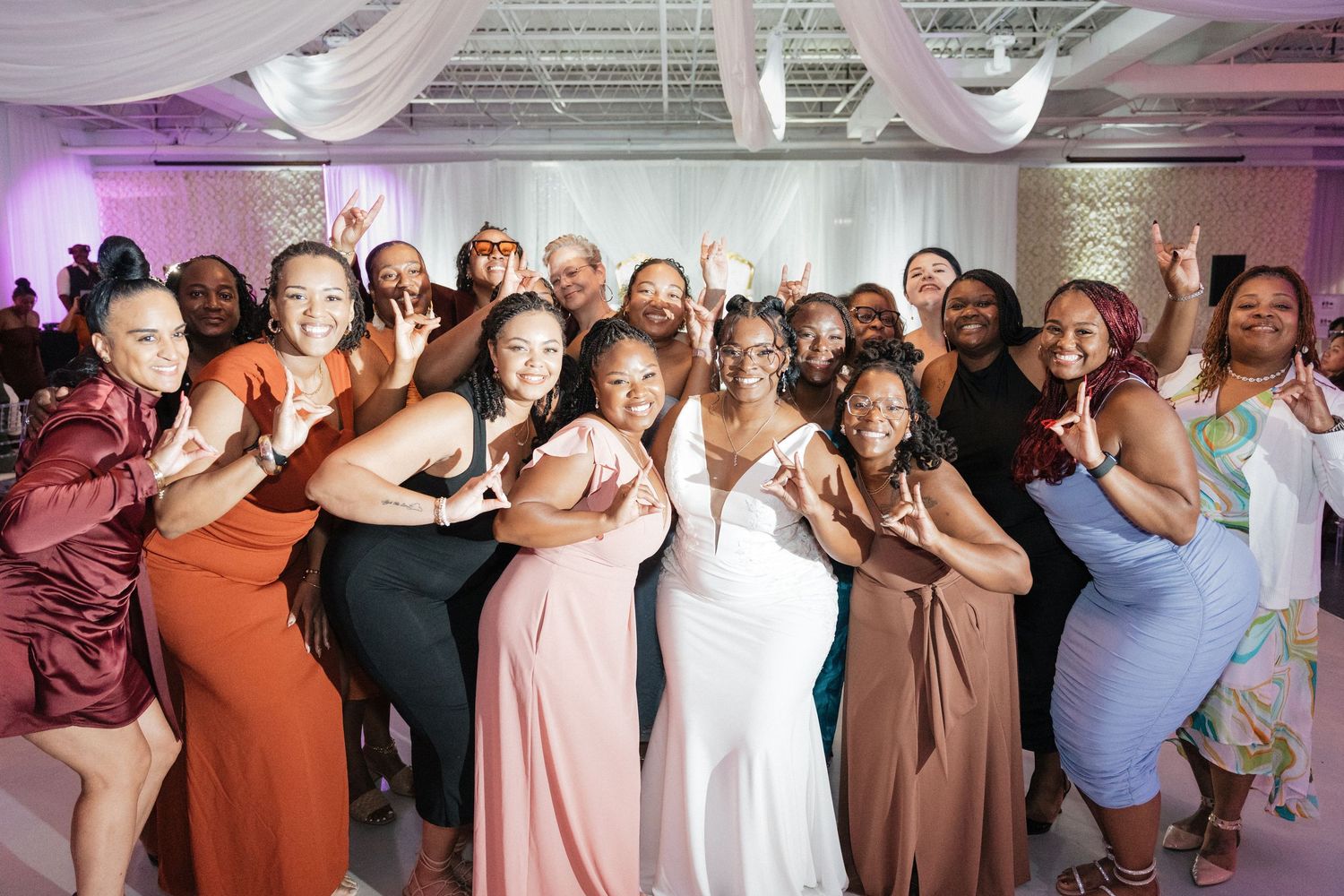 Wedding reception guests dance and celebrate together under purple mood lighting.