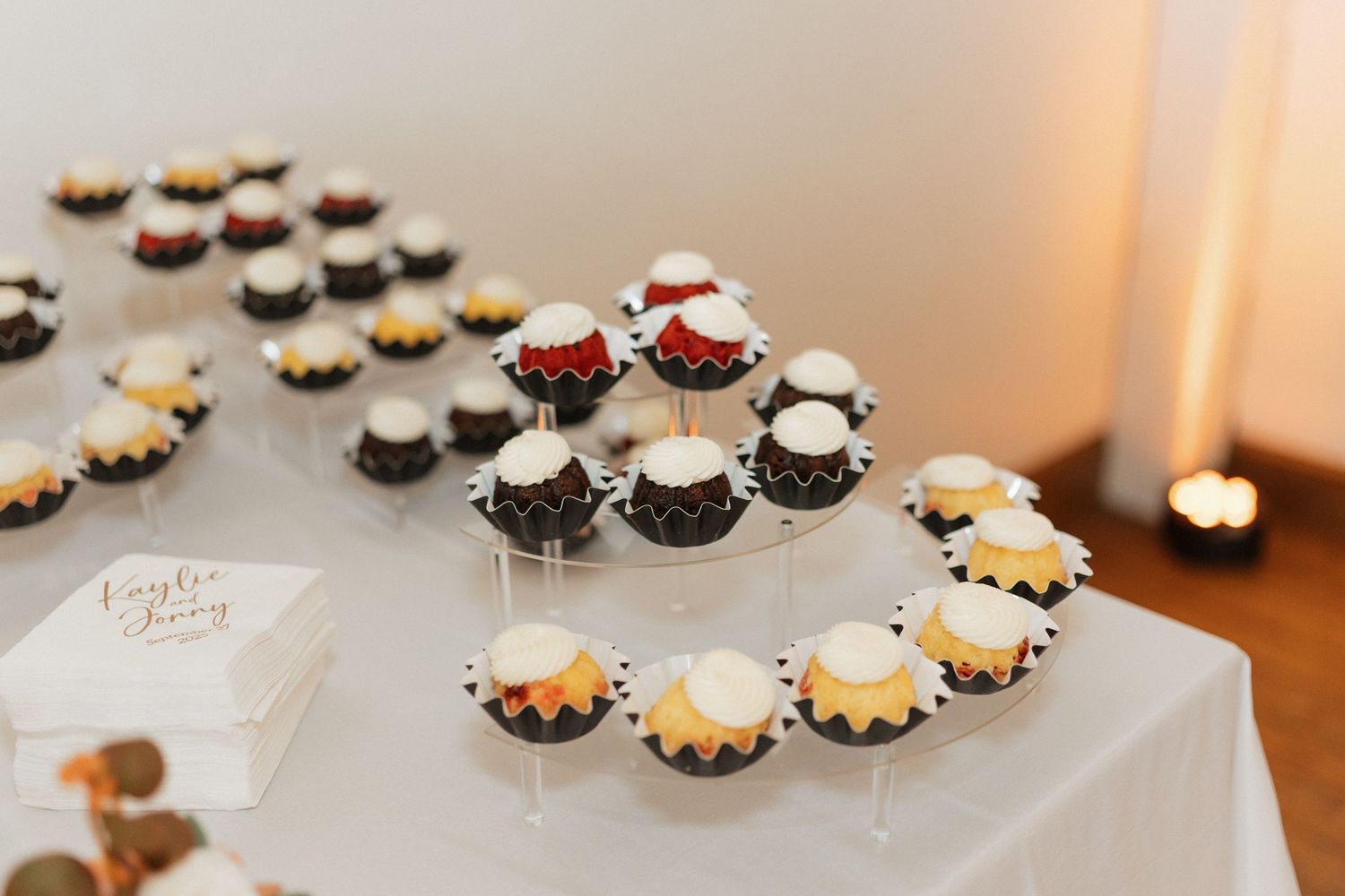 Display of elegant cupcakes and desserts arranged on white table at wedding reception.