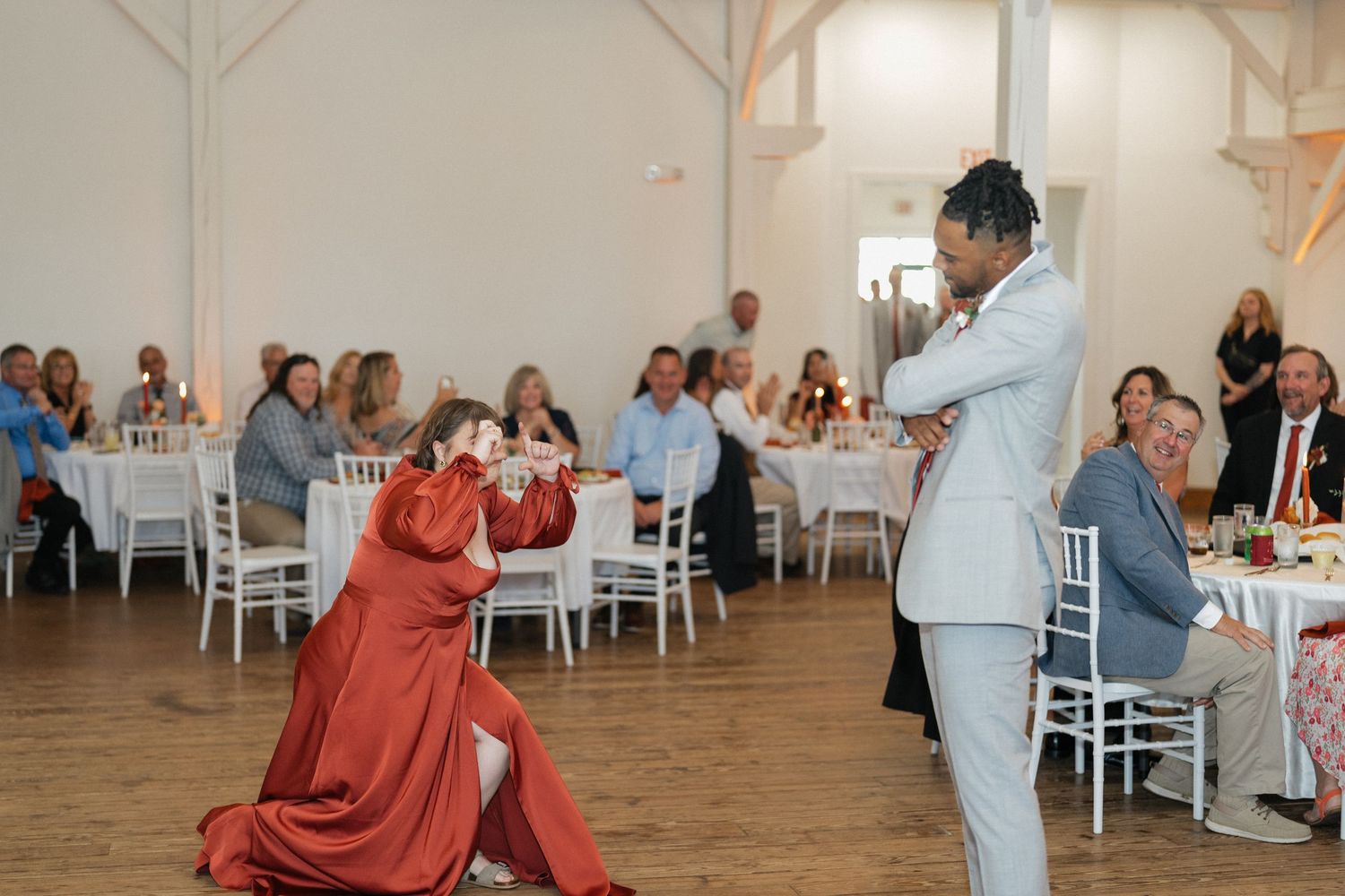 Wedding guests applauding during reception in elegant white barn venue.