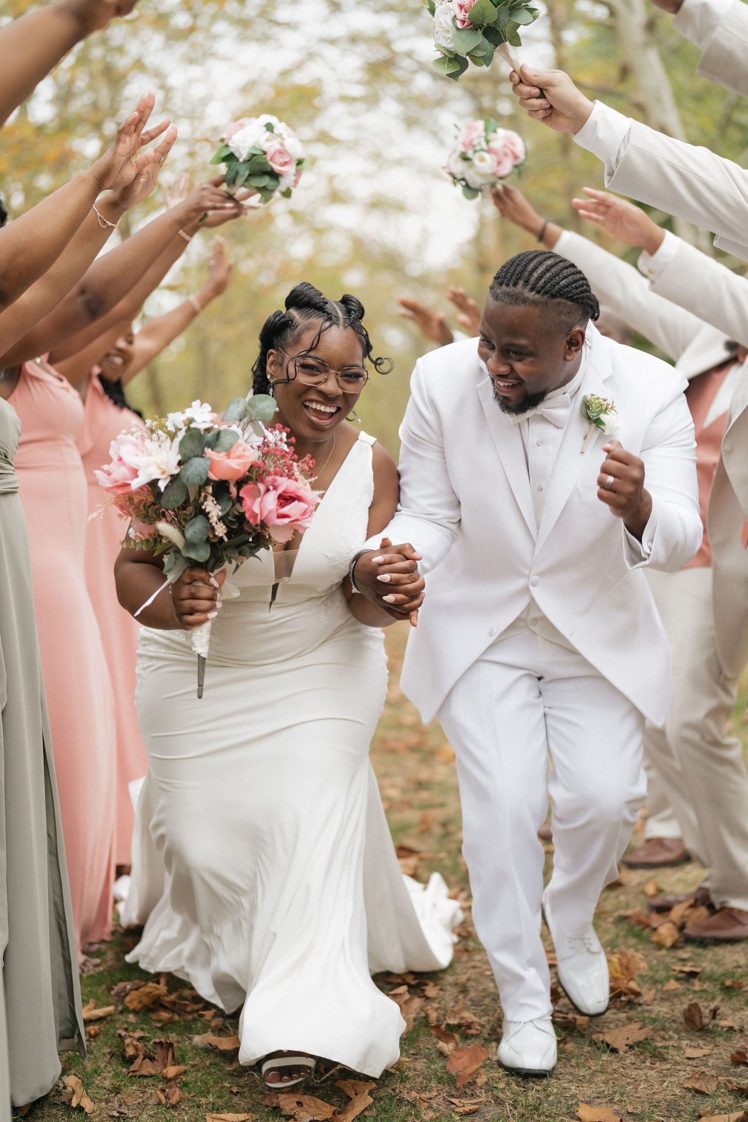 Wedding party celebrates joyfully outdoors with white and coral attire and floral bouquets.
