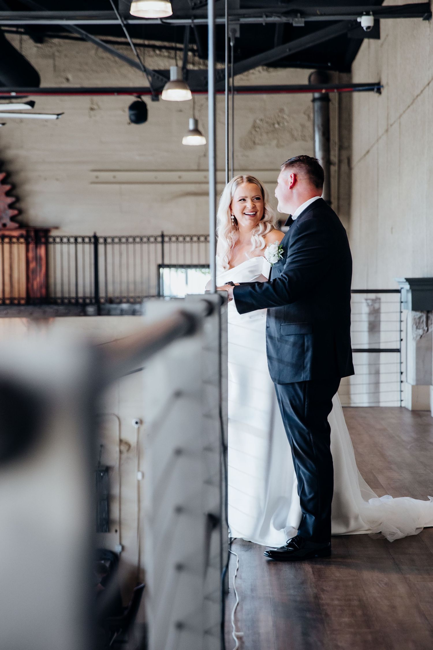 A couple shares an intimate moment during their first dance in an industrial-style venue with exposed ceiling and wood floors.