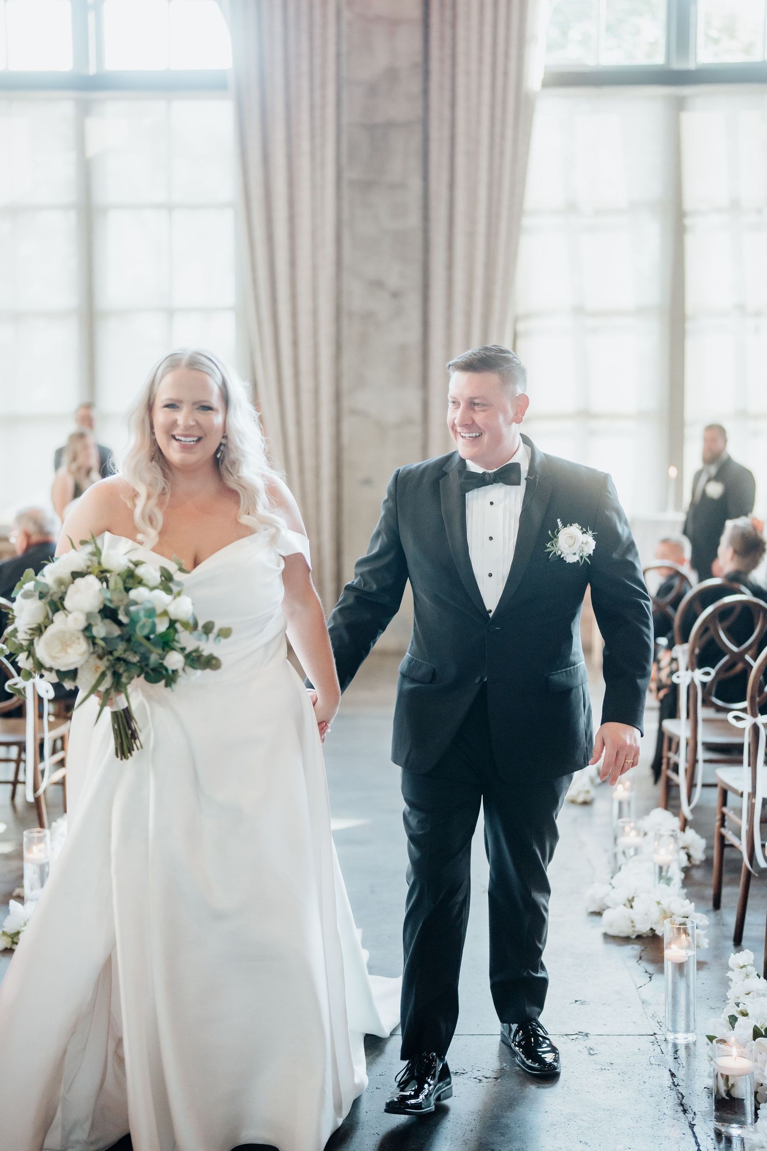 Elegant wedding reception setup in a bright ballroom with white decor and floral arrangements.