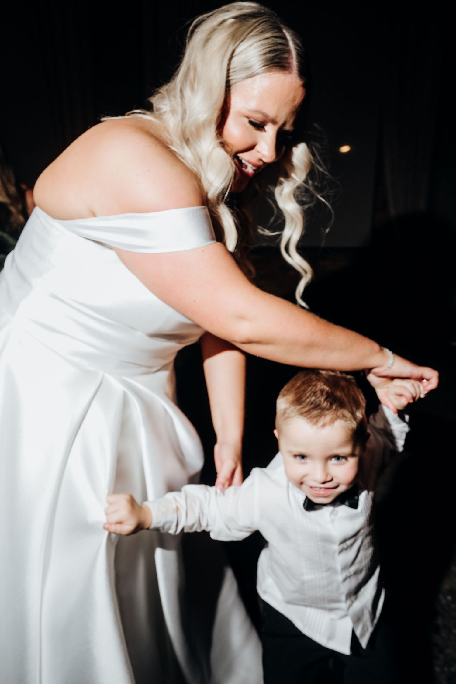 Bride in white dress dances with young child during wedding reception.