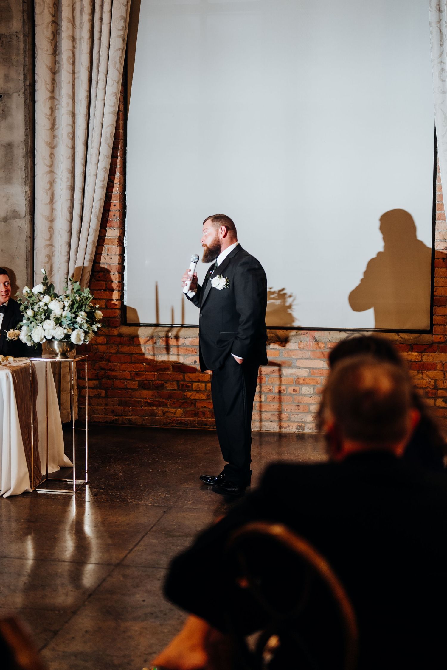 Wedding ceremony speech captured in dramatic lighting against exposed brick wall.