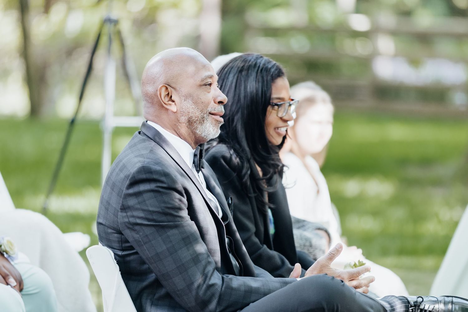 Wedding guests seated outdoors on white chairs during an outdoor ceremony.