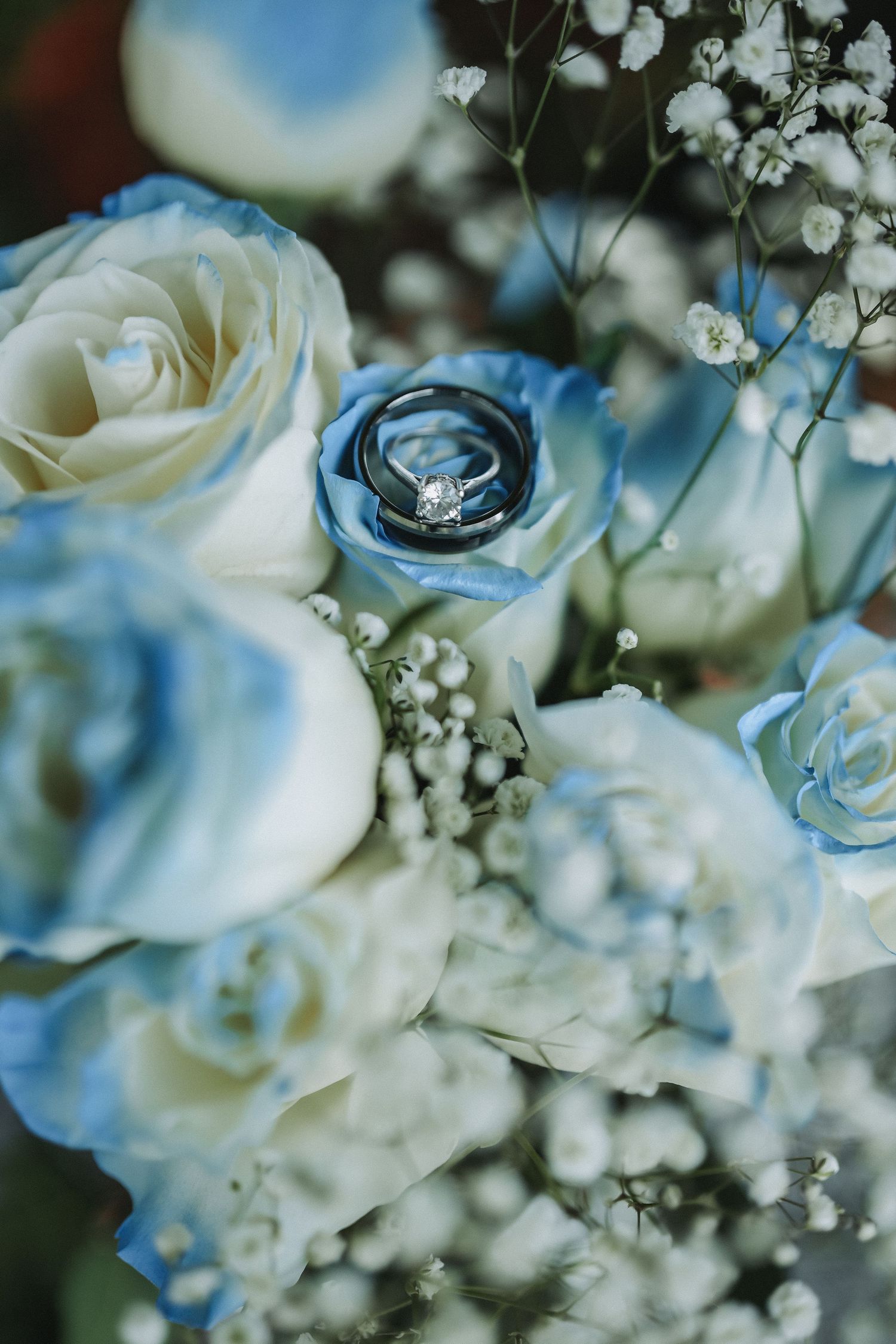 Wedding bouquet with white and blue roses featuring an engagement ring nestled in blue petals.