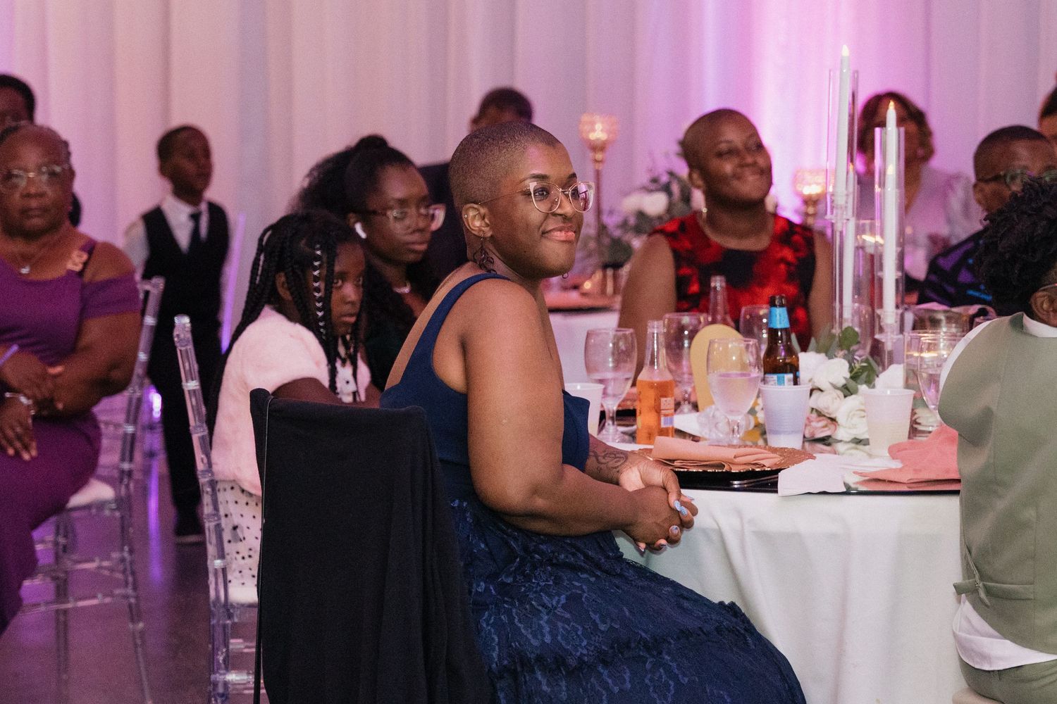 Wedding reception guests seated at elegant tables with pink lighting and candlelit decor.