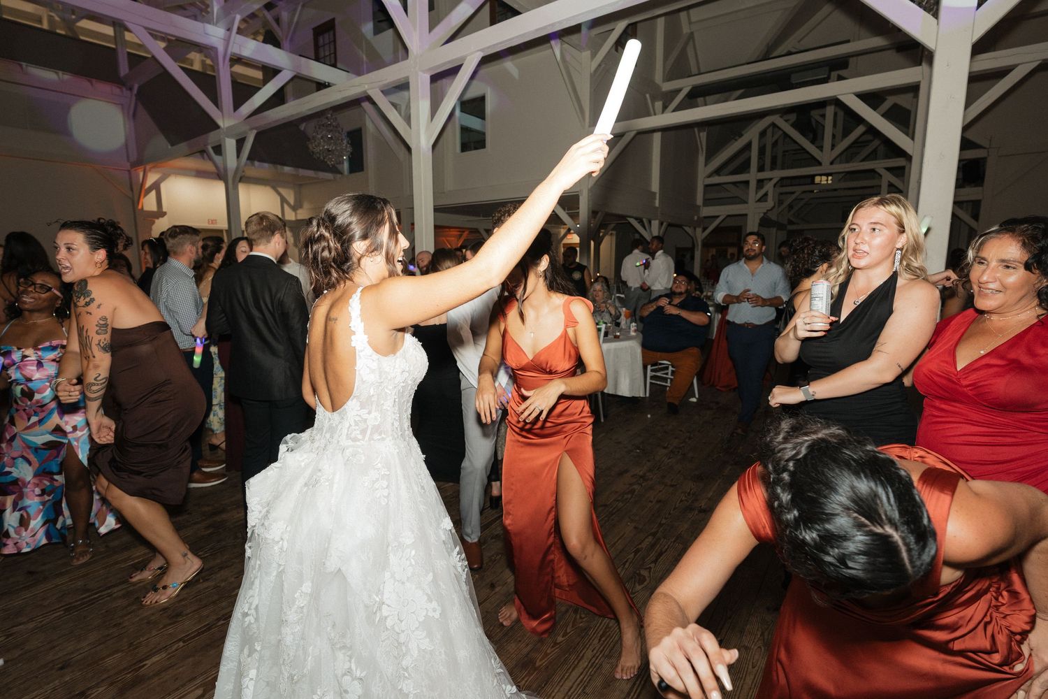 Wedding guests dancing and celebrating at indoor reception with rustic white beam ceiling.