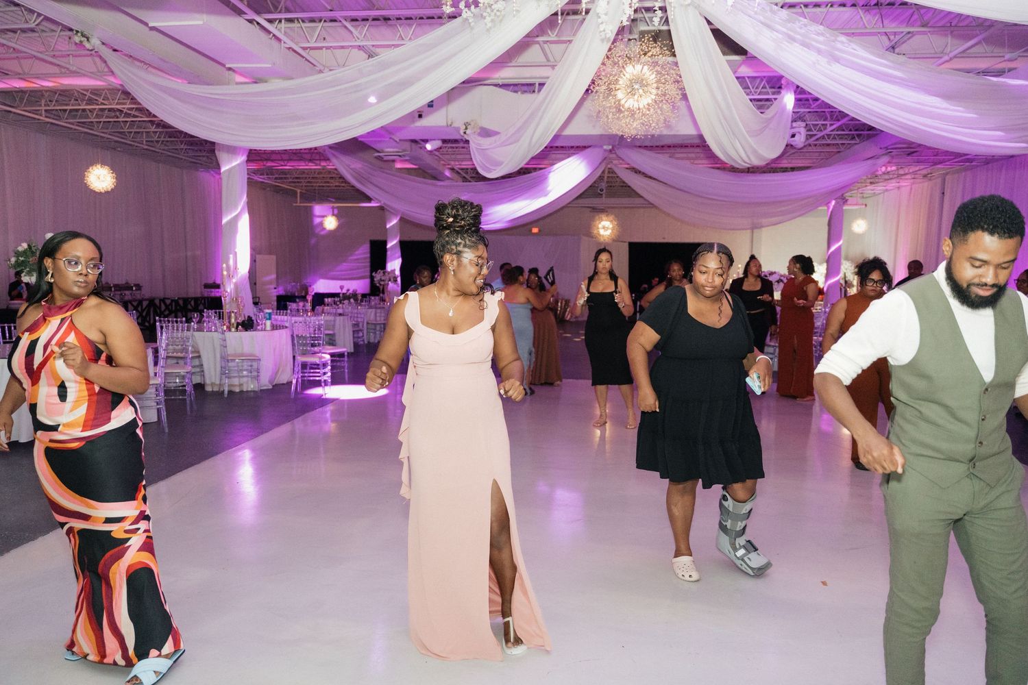Wedding guests dance and socialize on a white dance floor with purple ambient lighting.