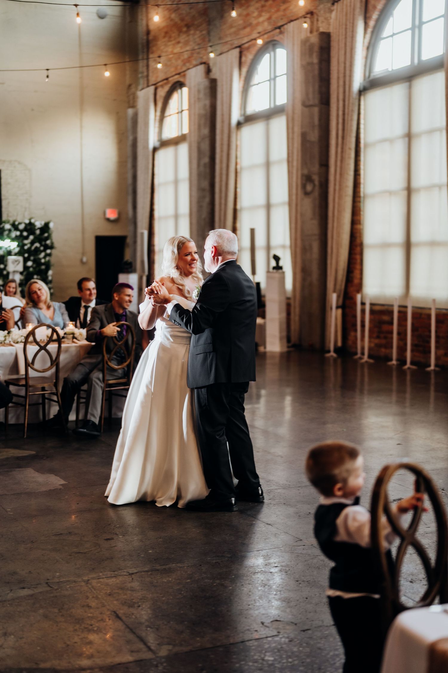 A wedding reception in a rustic venue with brick walls and arched windows.