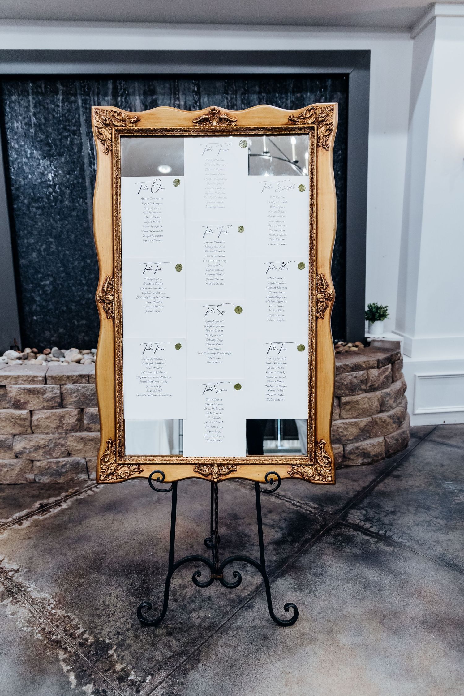 Gold framed menu signs on black metal easels displayed against stone and gray wall.
