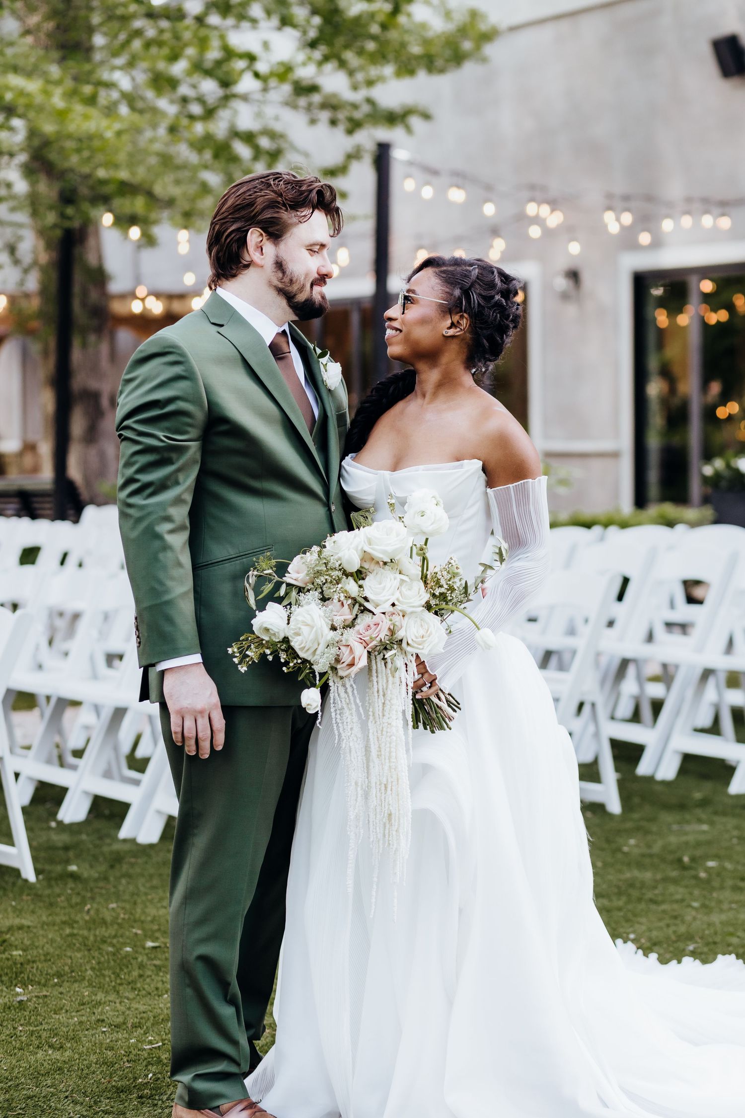 Wedding ceremony setup with white chairs and string lights in outdoor garden setting.