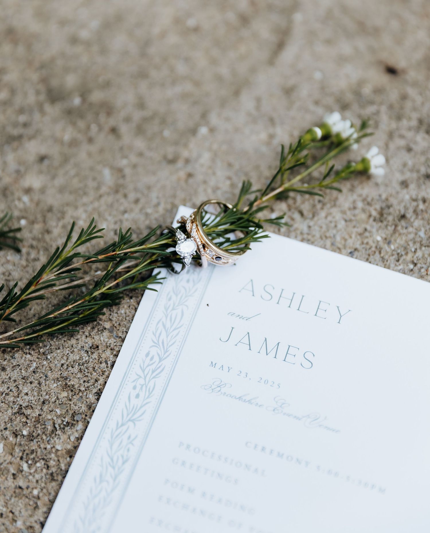 Wedding invitations with elegant script font and greenery details laid out on a textured concrete surface.
