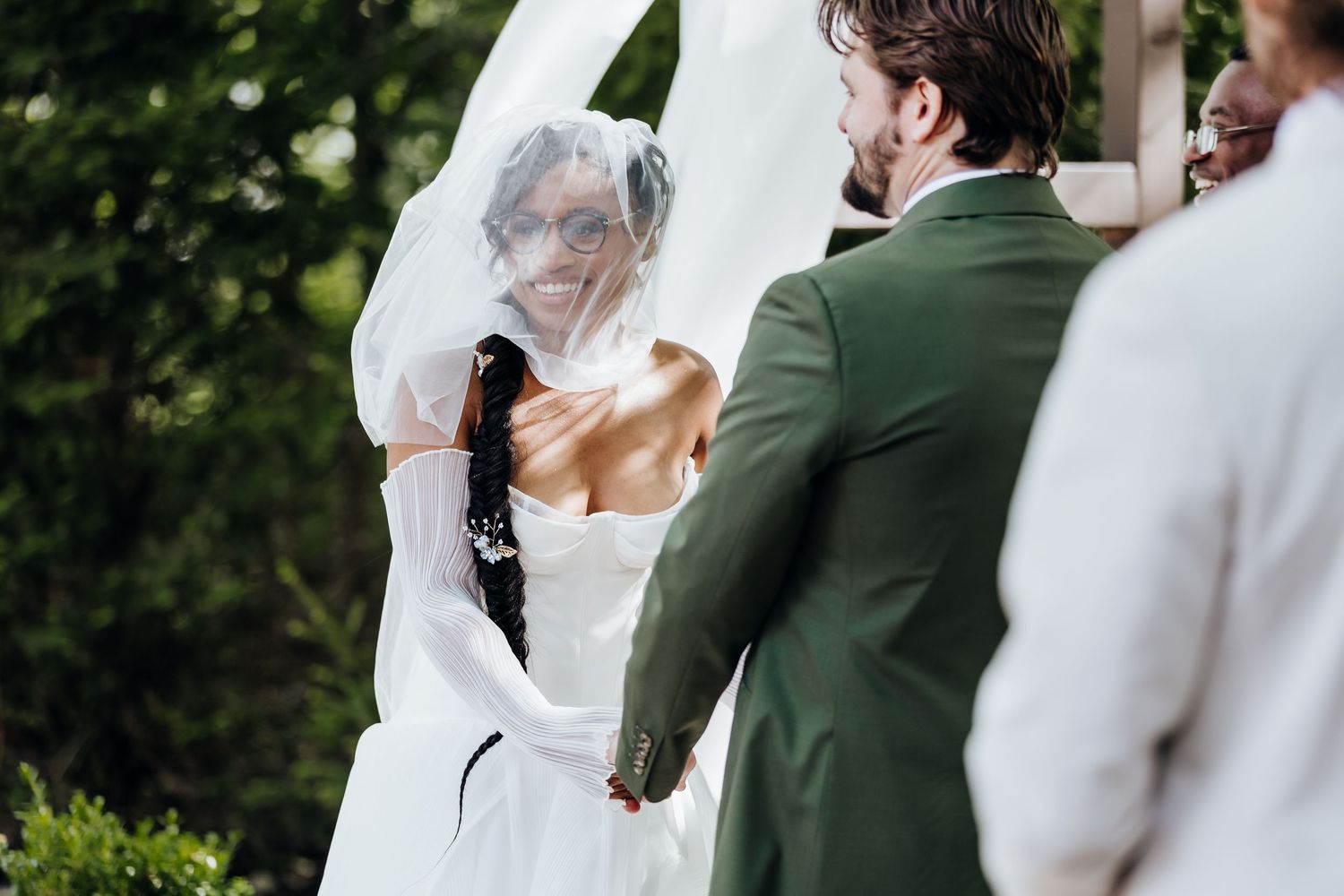 An outdoor wedding ceremony scene with attendees gathered under trees.